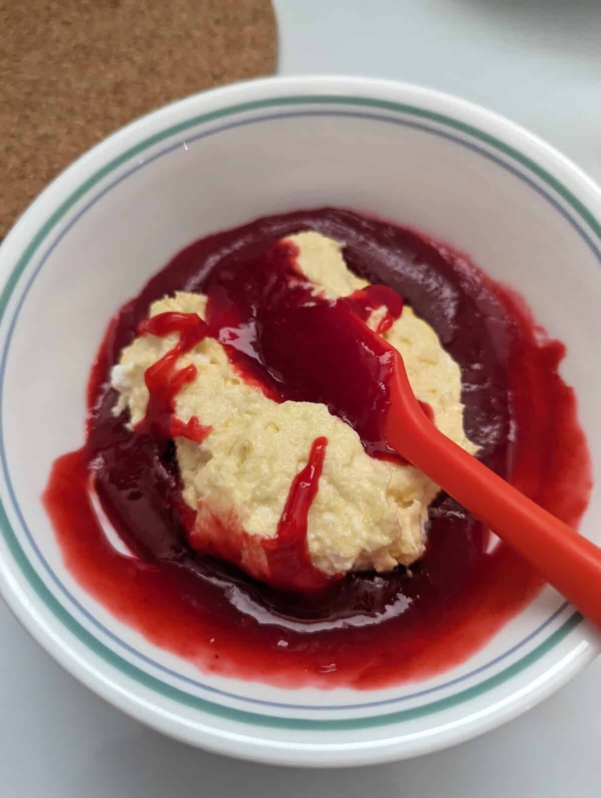 Cake batter being folded into raspberry coulis mixture in a white bowl.