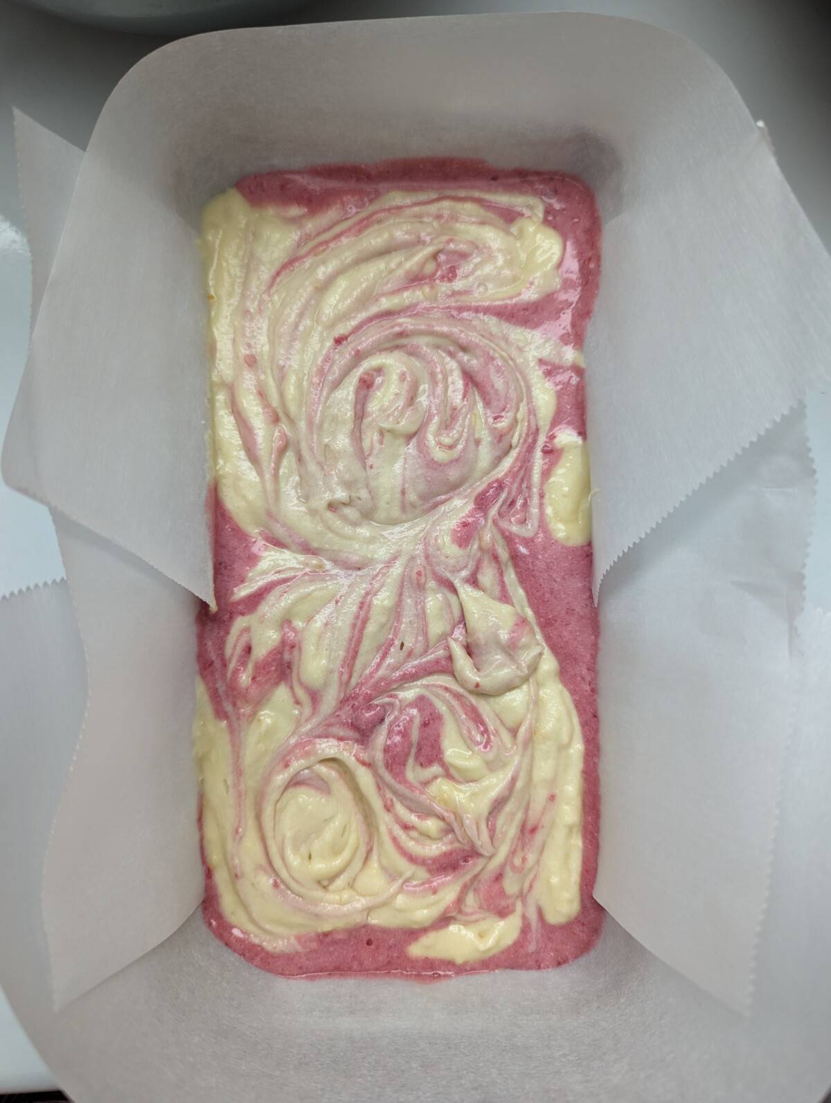 Swirled raspberry pink and yellow cake batter in a loaf pan.
