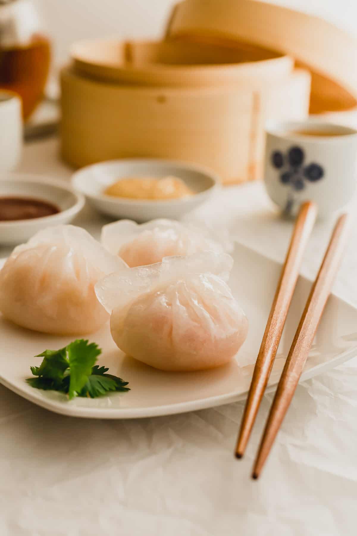 Steamed shrimp har gow dumplings on a white plate with chopsticks.
