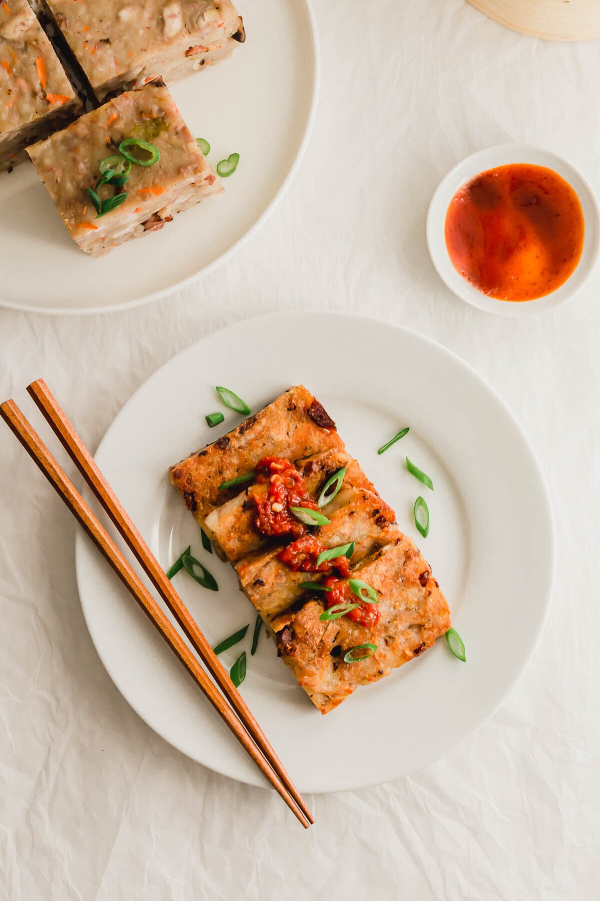 Slices of pan-fried taro cake on a white plate, with chopsticks on the side.