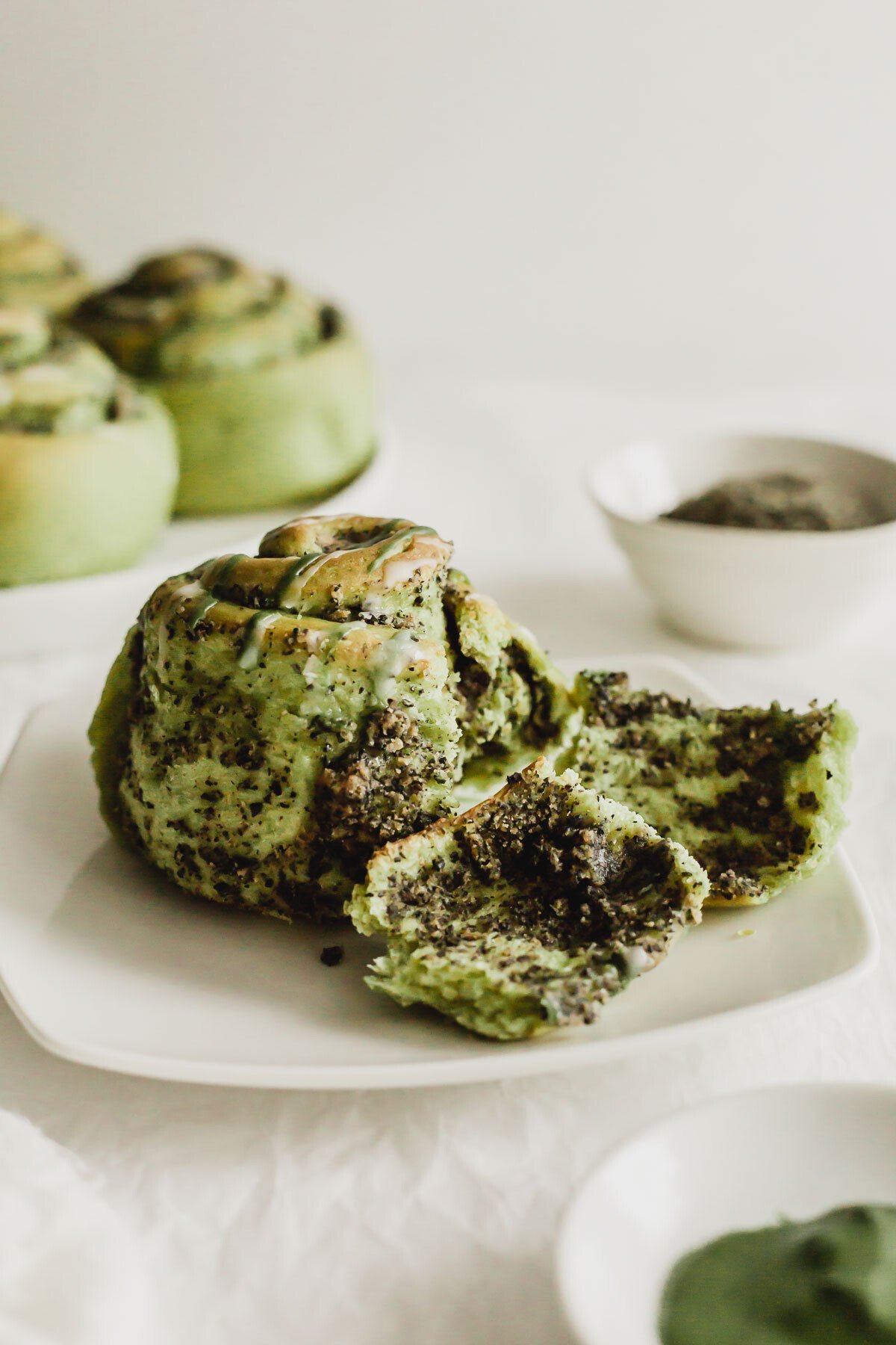 A torn open matcha black sesame cinnamon bun on white square plate.