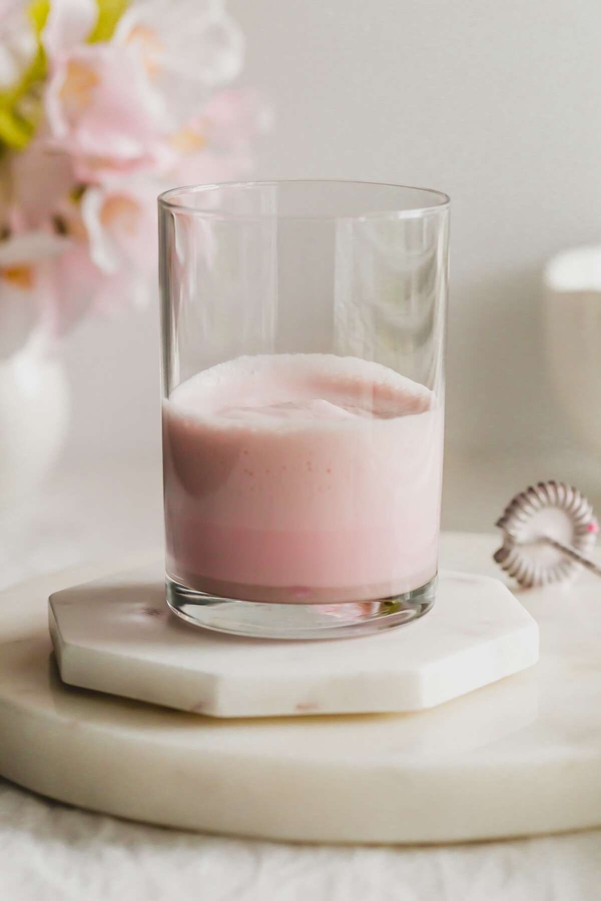 Glass of sakura cold foam cream on stacked white marble coasters.