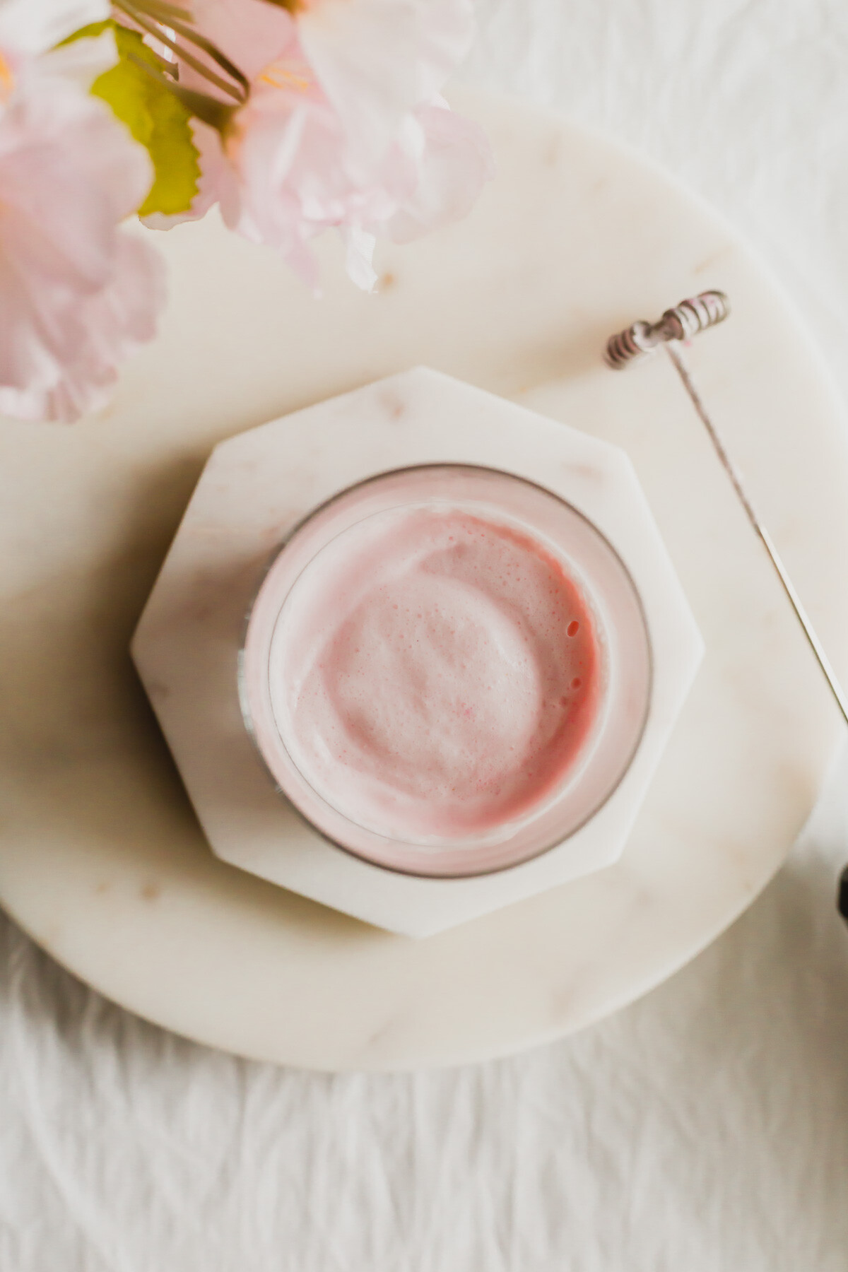 Glass of sakura cold foam cream on stacked white marble coasters, with electric frother on the side.