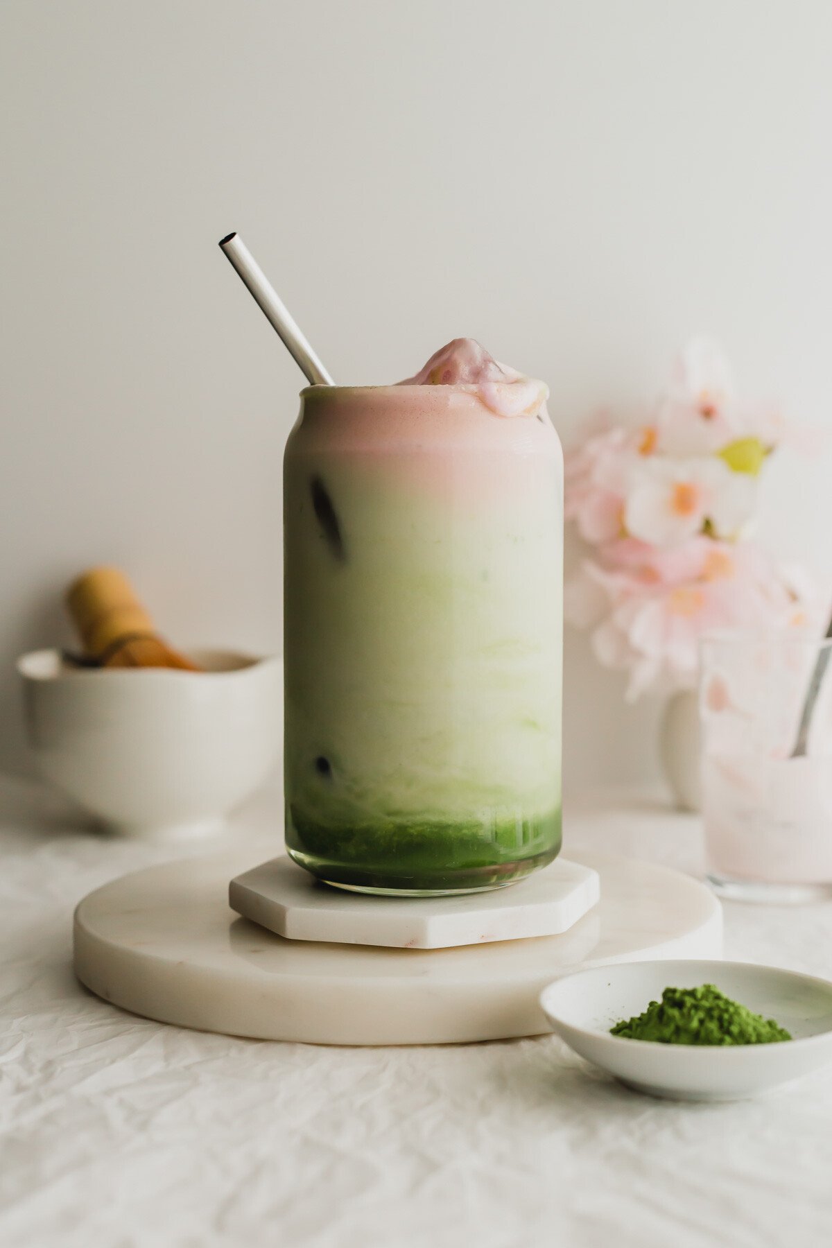 A glass of sakura matcha latte, with stainless steel straw, on white marble coasters.