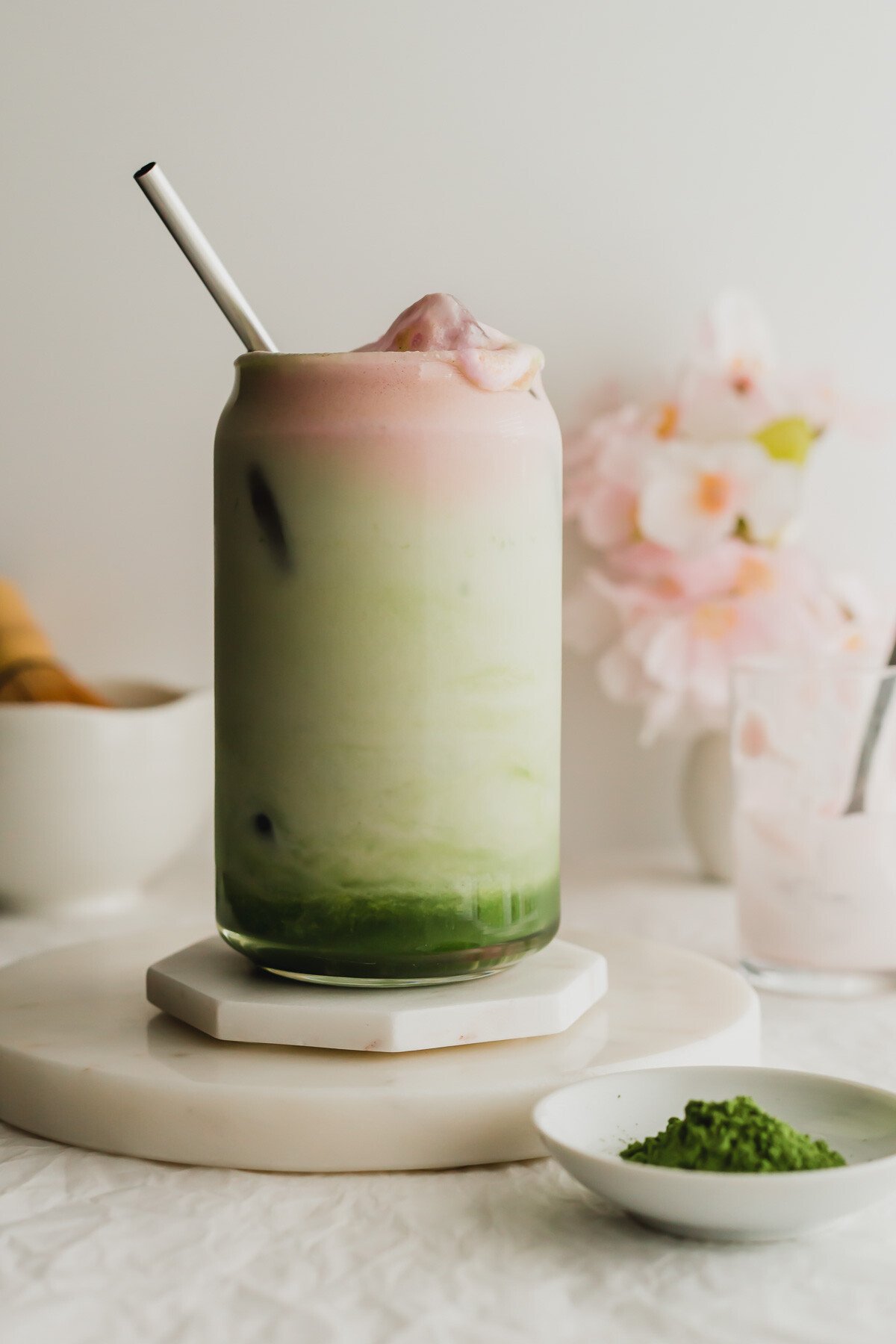 A glass of sakura matcha latte, with stainless steel straw, on white marble coasters.