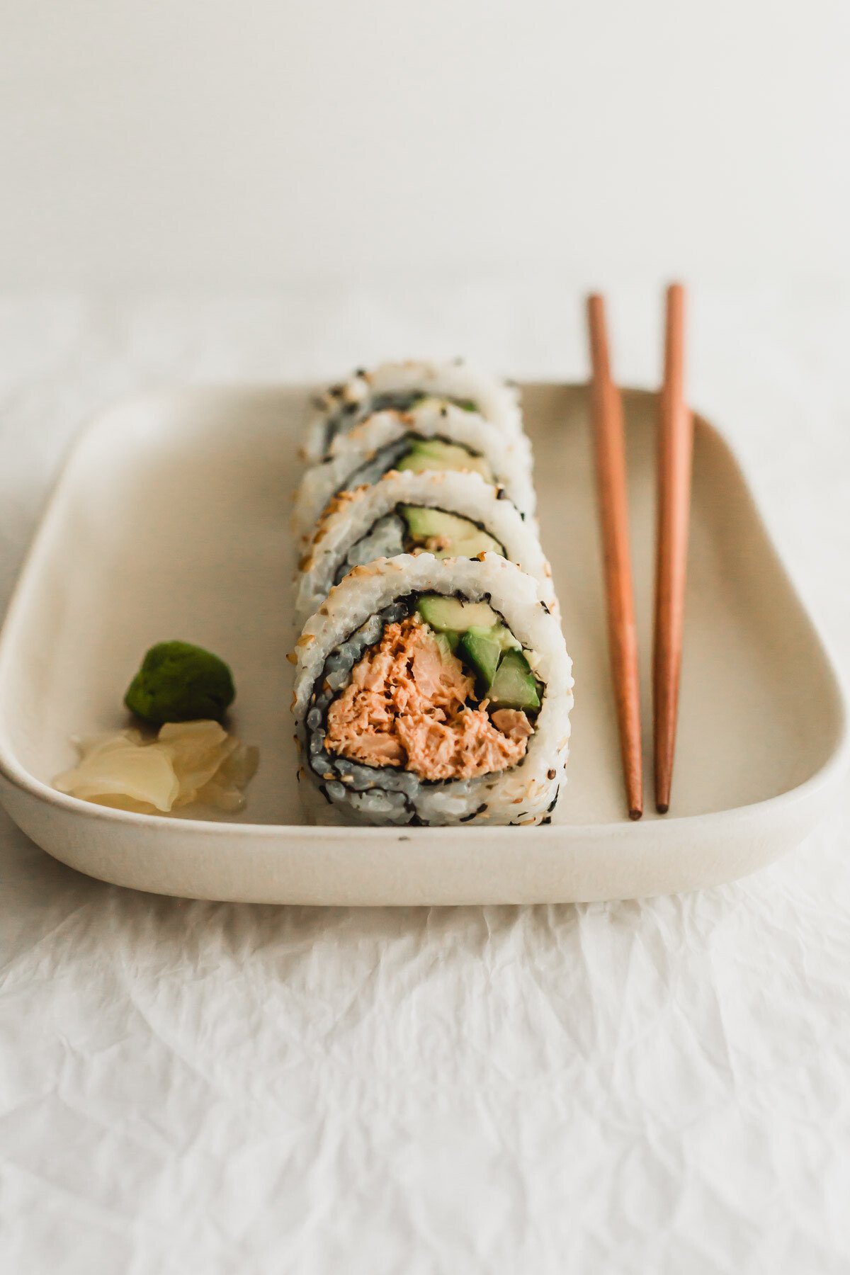 Cooked spicy tuna sushi rolls on a beige rectangular plate with wooden chopsticks on the side.