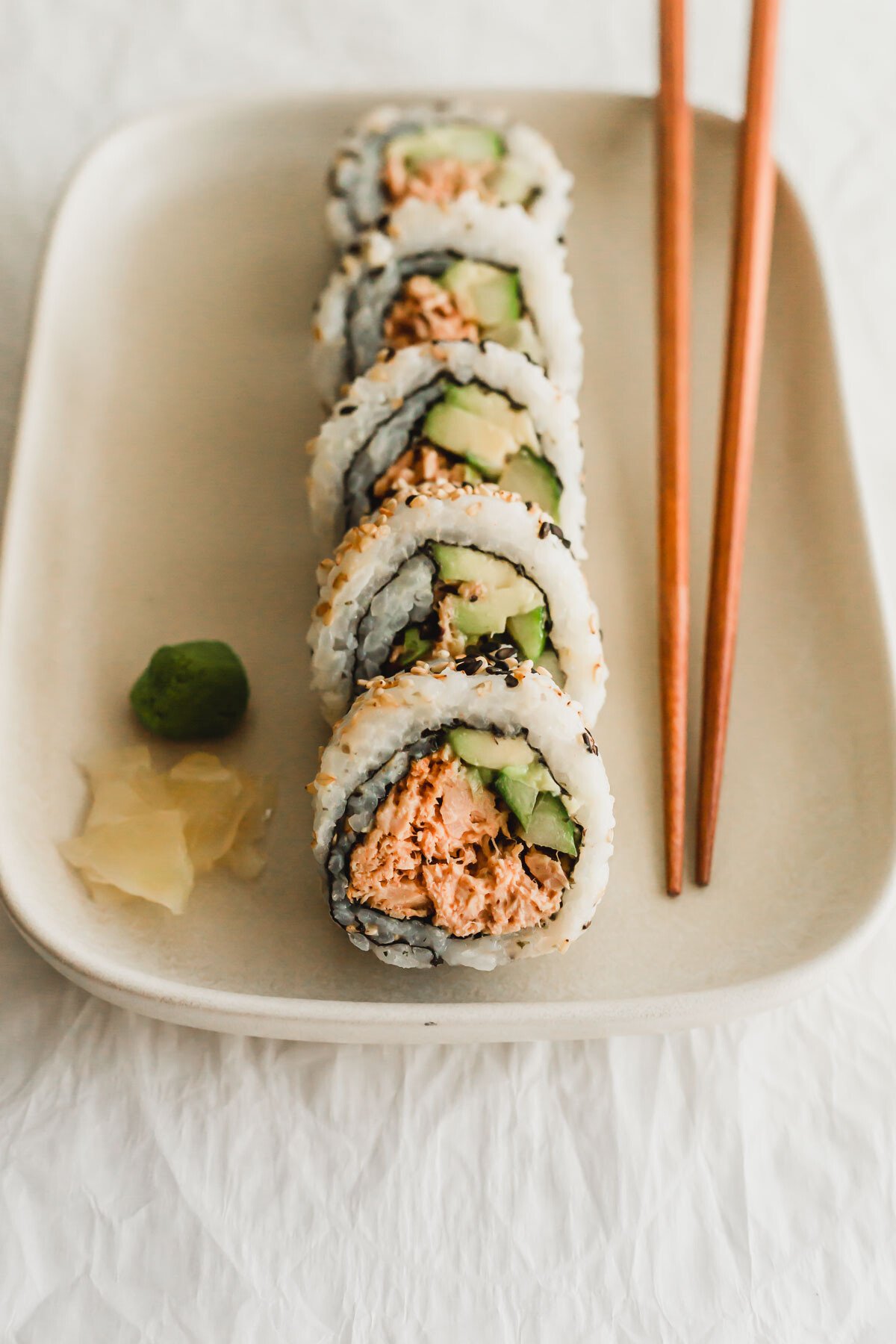 Spicy tuna sushi rolls on a beige rectangular plate with wooden chopsticks on the side.