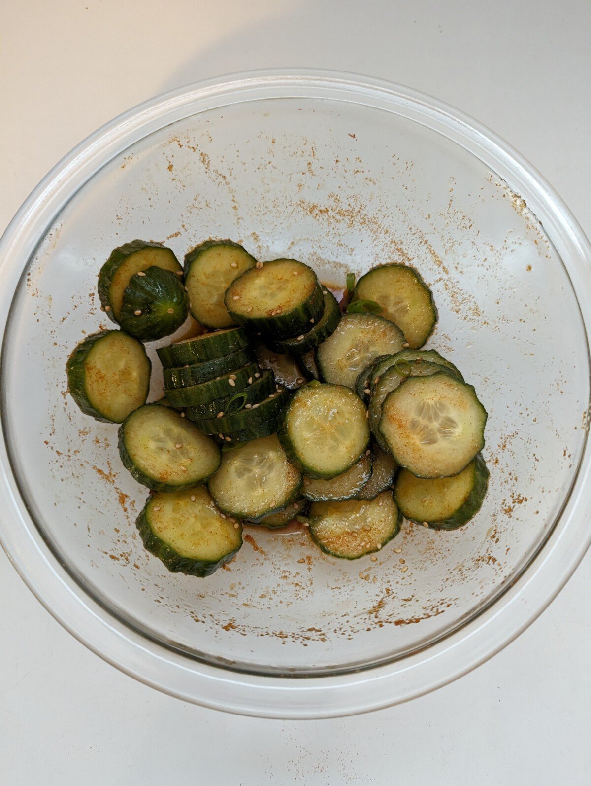 Sliced cucumbers mixed with seasonings in a glass bowl.