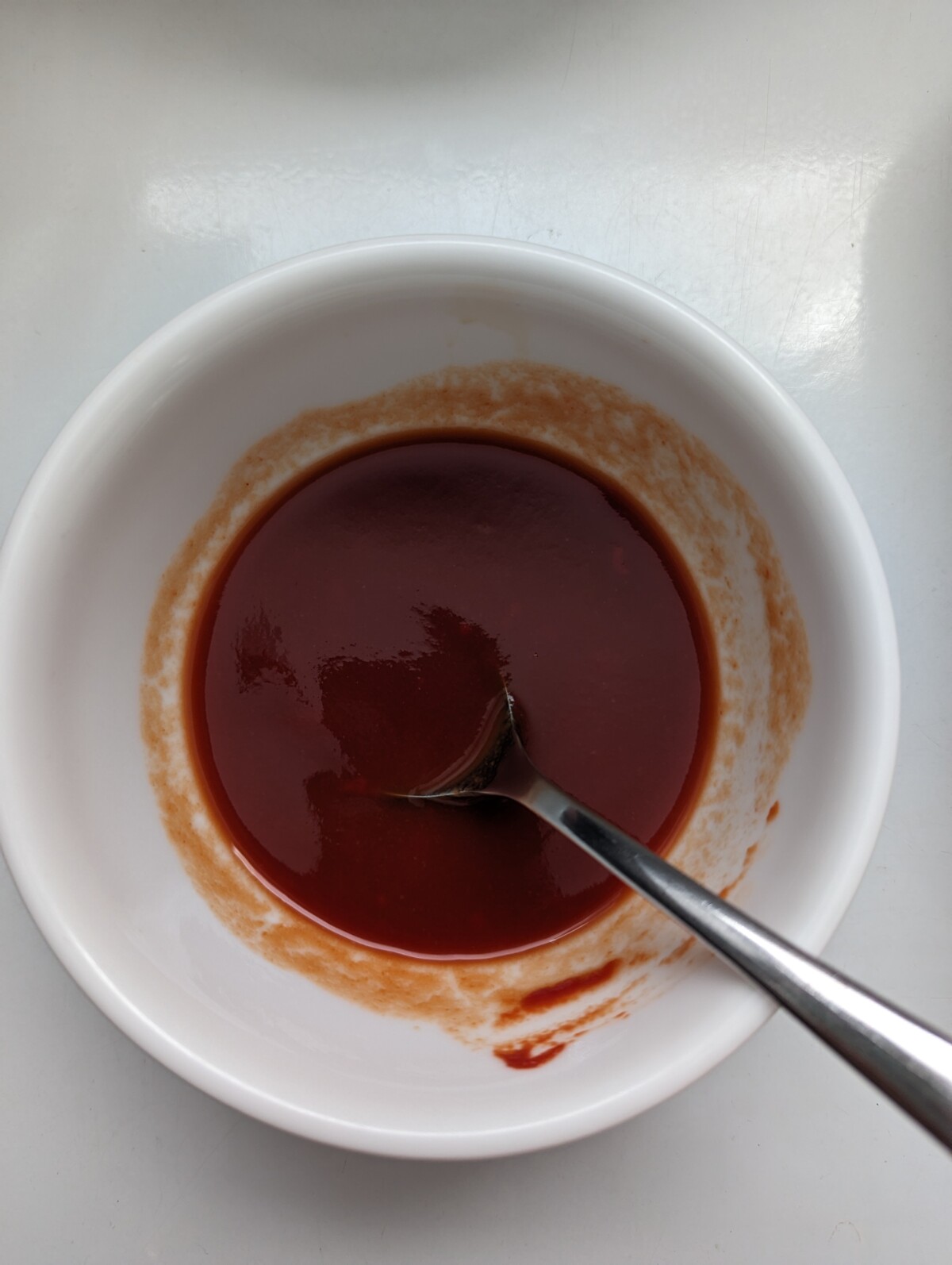 A white bowl with red tomato sauce and spoon.