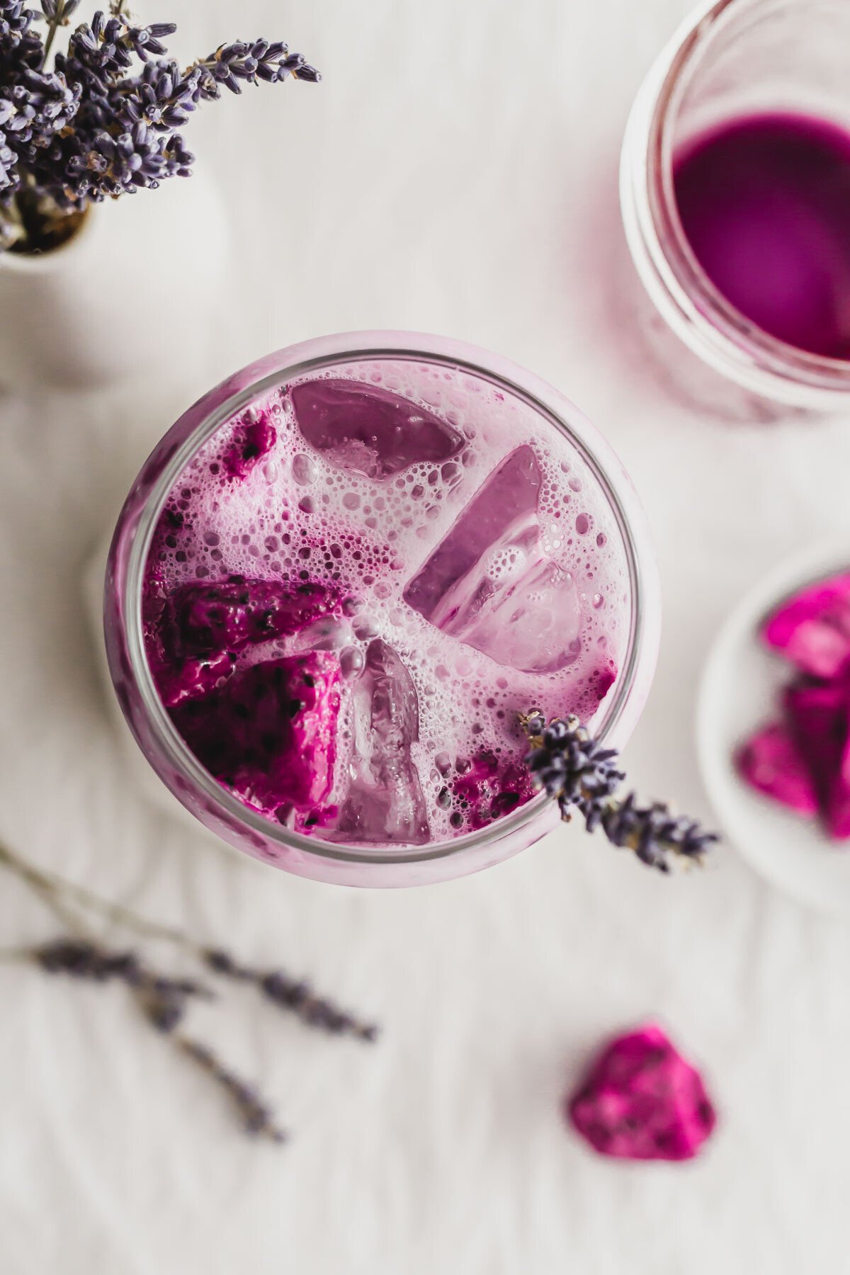 Lavender oat milk with dragonfruit with ice cubes in a glass, with lavender sprig sticking out.