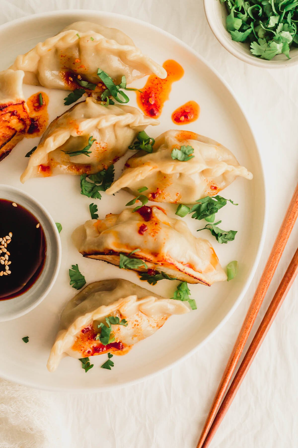 Chinese lamb dumplings on a white plate, drizzled with chili oil.