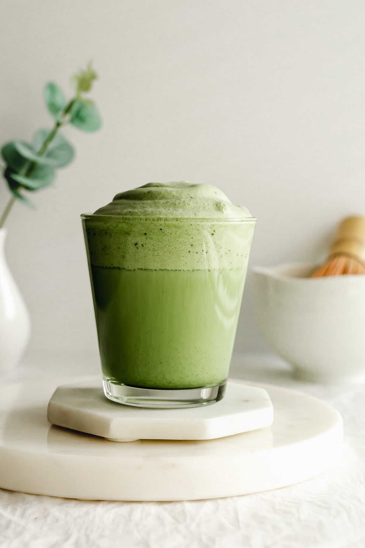 Matcha cold foam in a glass on white marble coasters.