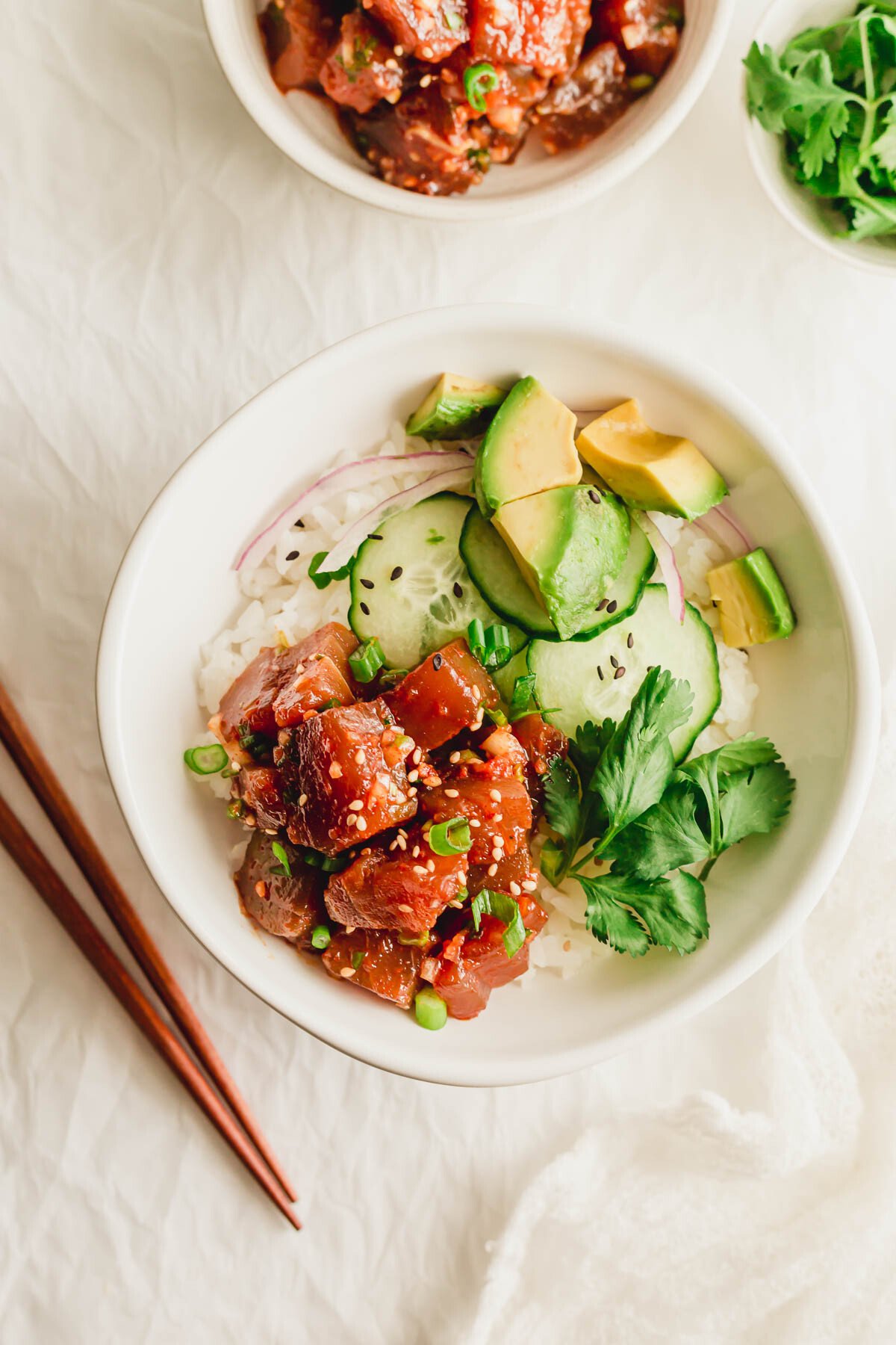 A white bowl of rice with spicy tuna poke and vegetables.
