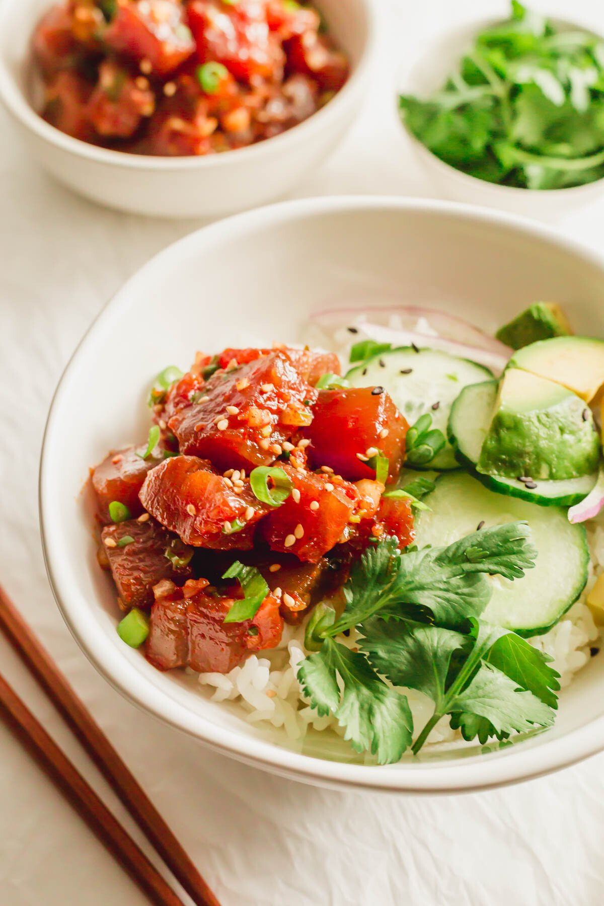 A white bowl of rice with spicy tuna poke and vegetables.