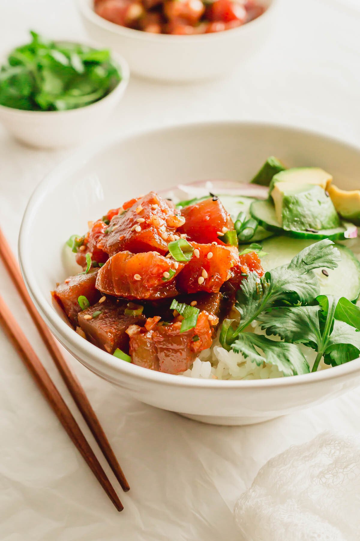 A white bowl of rice with spicy tuna poke and vegetables.
