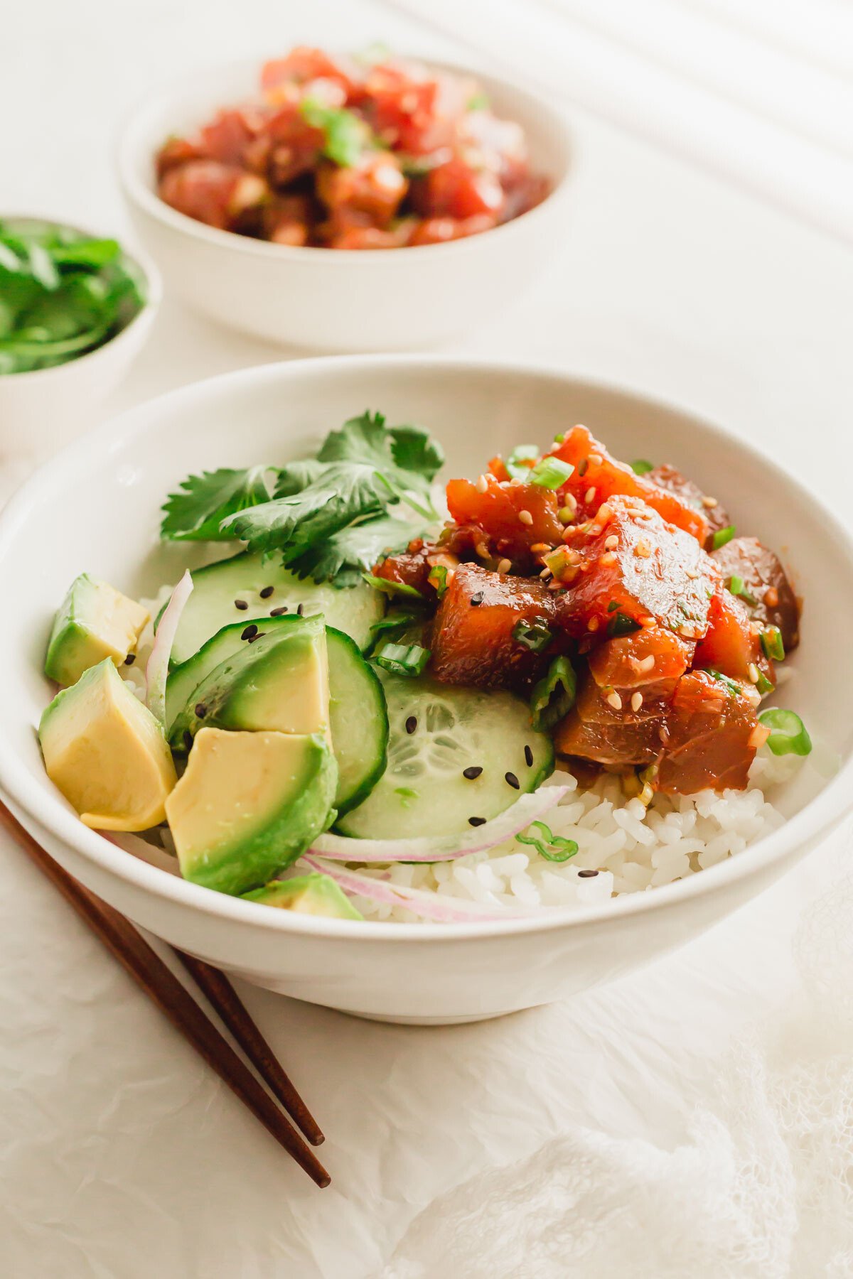 A white bowl of sushi rice with spicy tuna poke and vegetables.