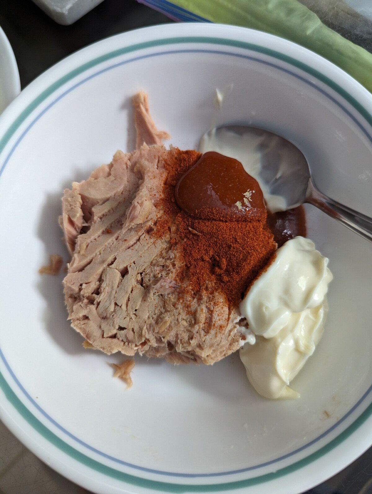 Canned tuna with chili sauce and seasonings in a white bowl with spoon.