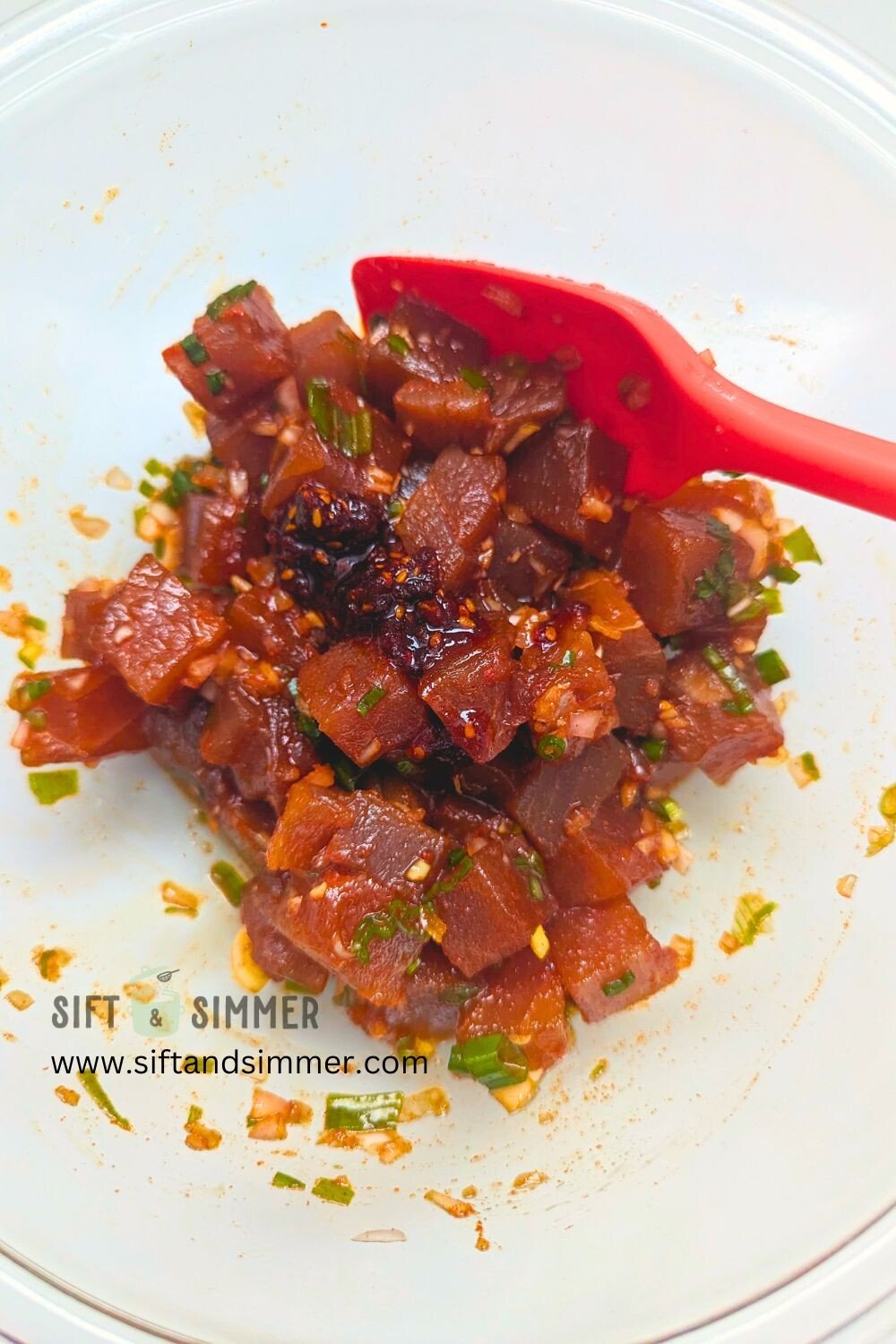 Cubed tuna with spicy seasonings and aromatics in a glass bowl.