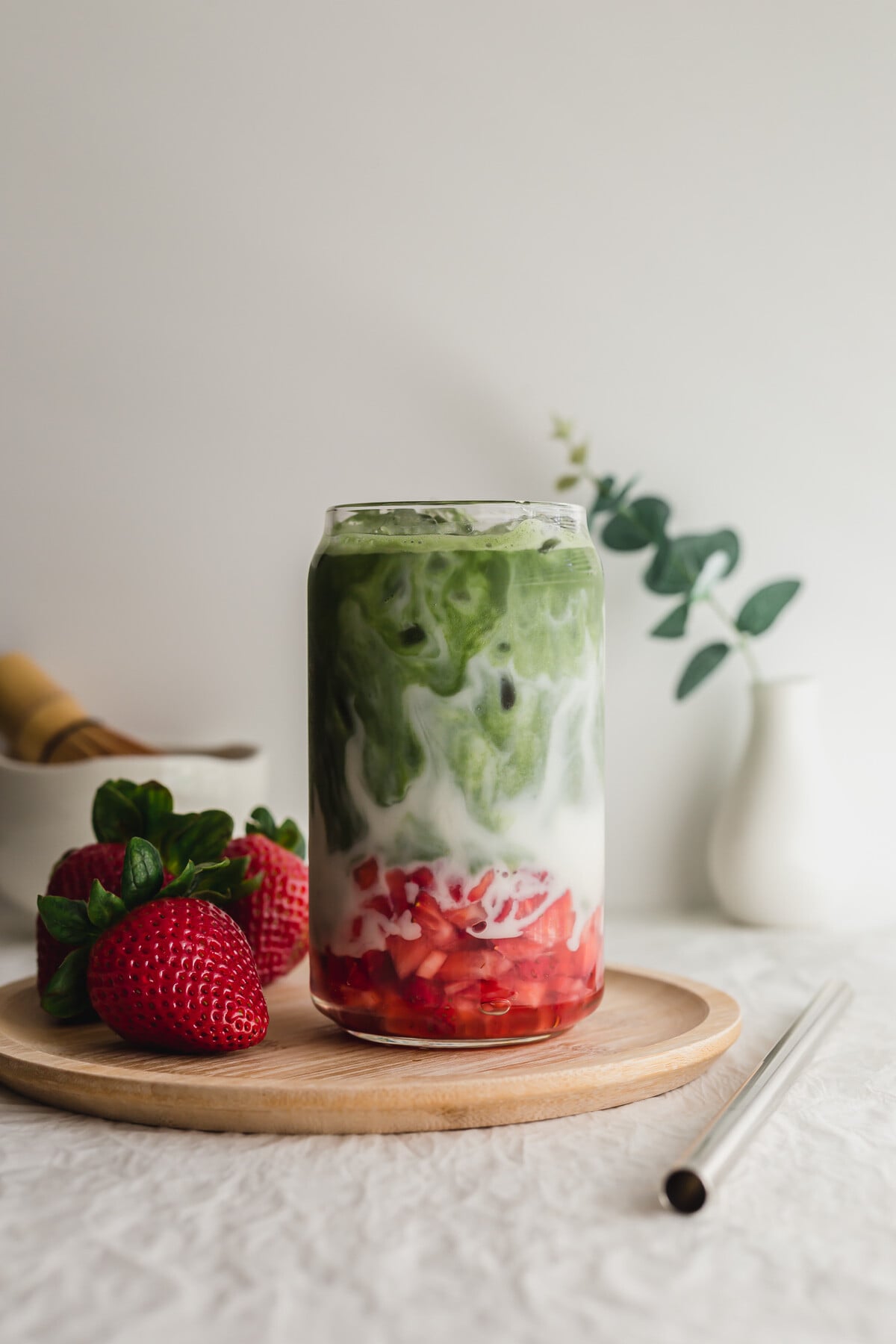 Matcha strawberry latte in a glass on a wooden plate.