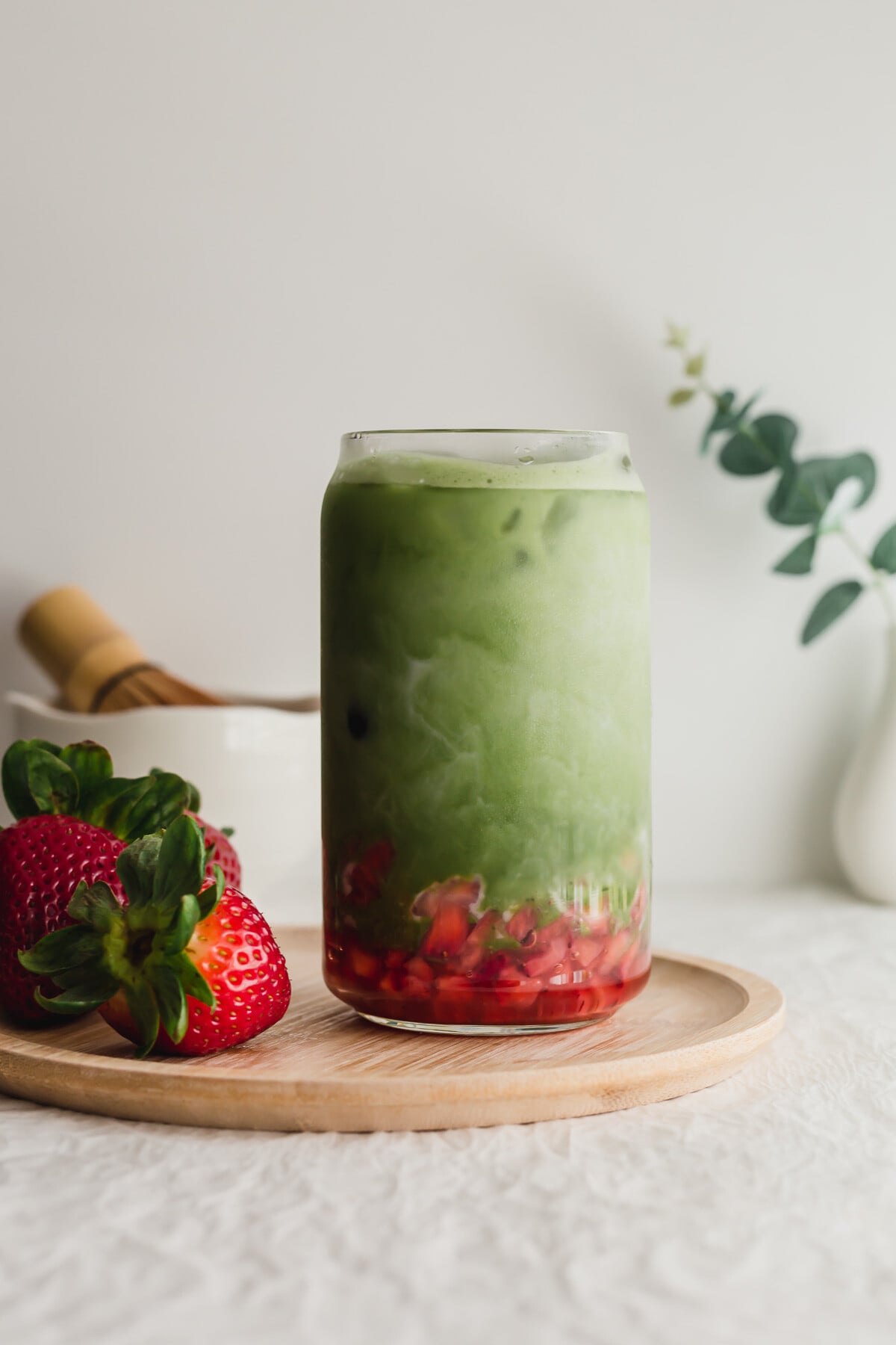 Stirred matcha strawberry latte in a glass on a wooden plate.
