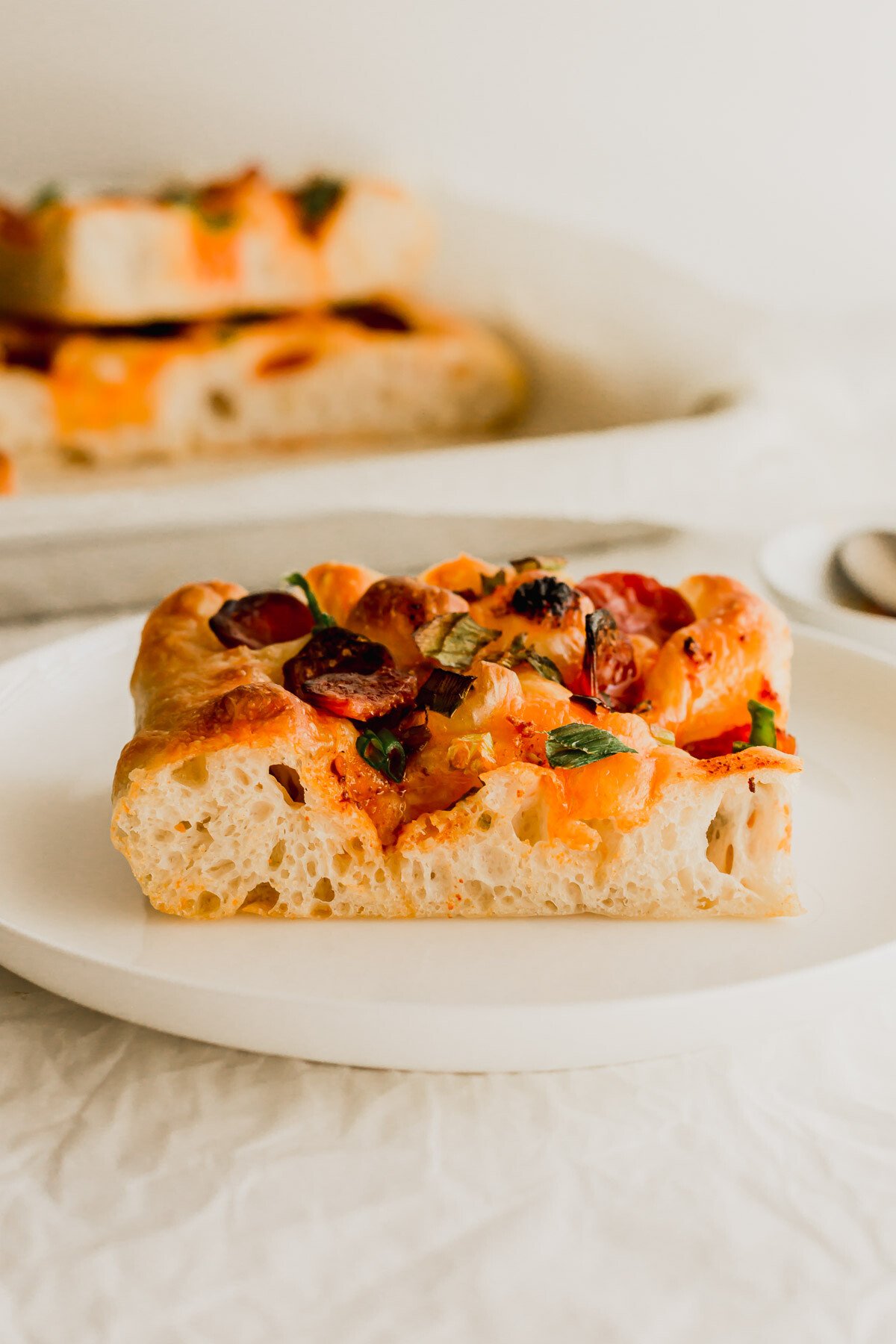 A slice of chili oil focaccia with Chinese sausage on a white plate.