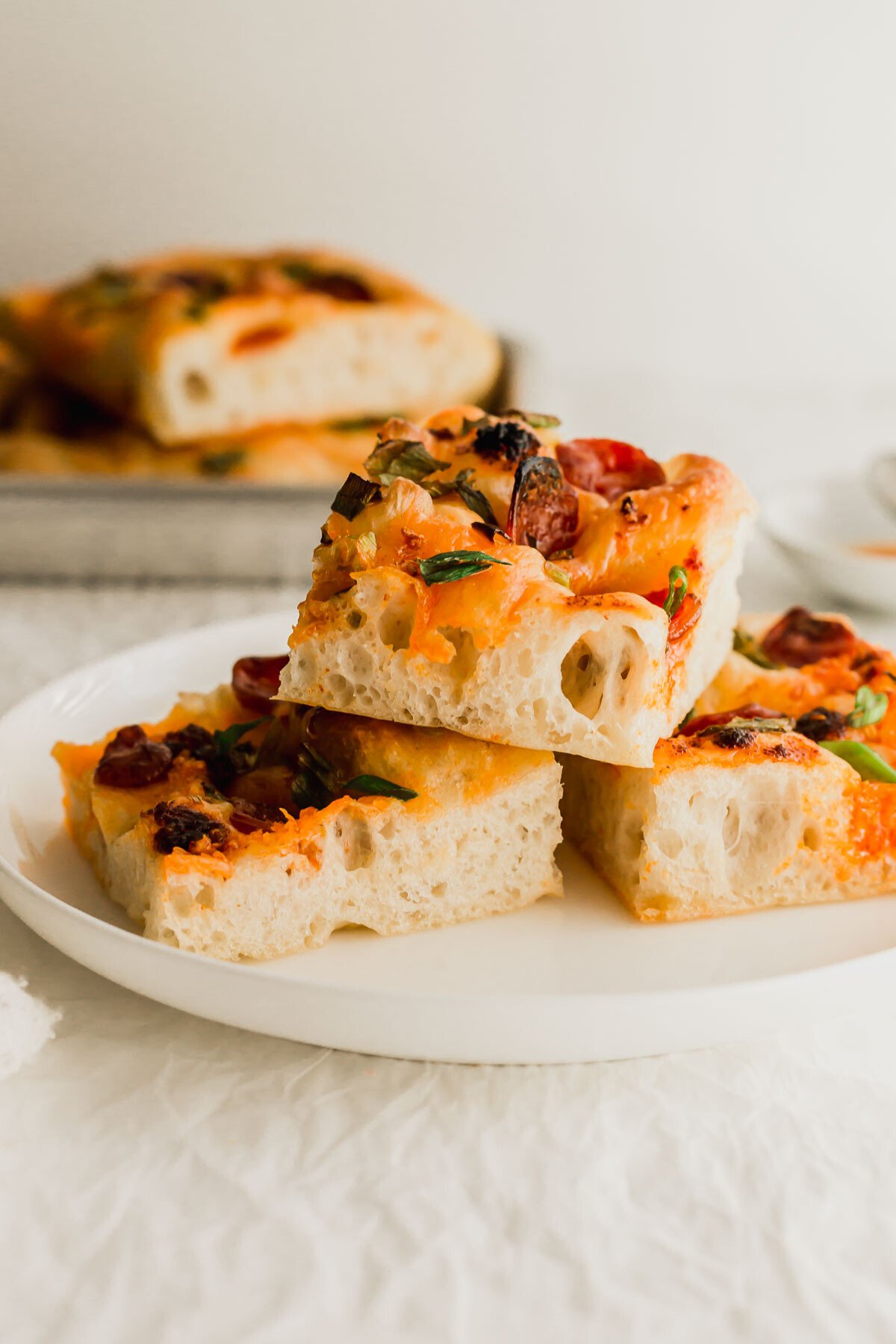 Slices of of chili oil focaccia with Chinese sausage piled on a white plate.
