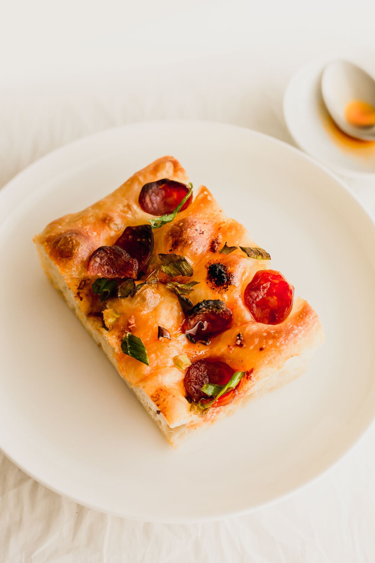 A slice of chili oil focaccia with Chinese sausage on a white plate.