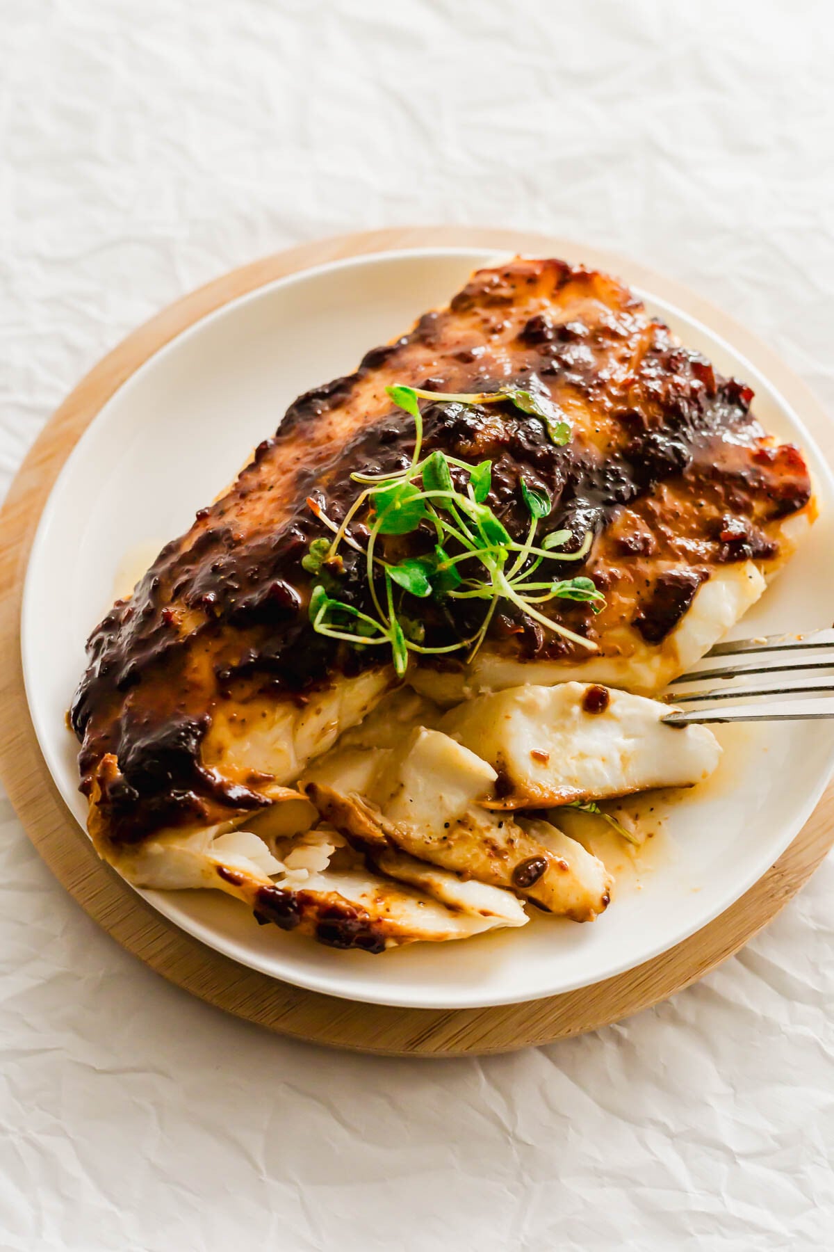 Flaked Hoisin glazed cod on a white plate, with fork.