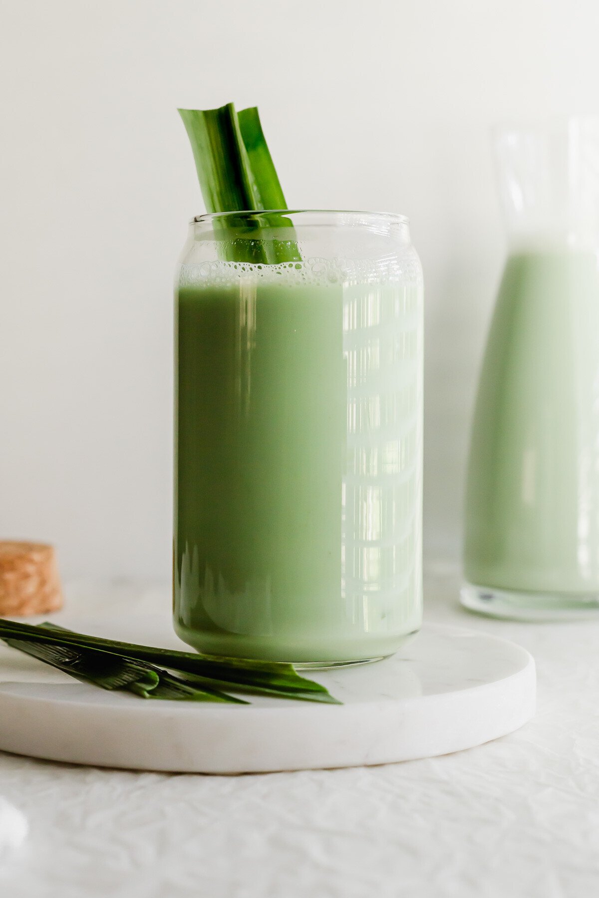 A glass of pandan soy milk on white round marble.