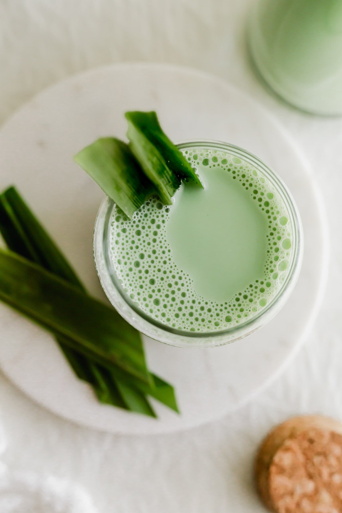 A glass of pandan soy milk on white round marble.