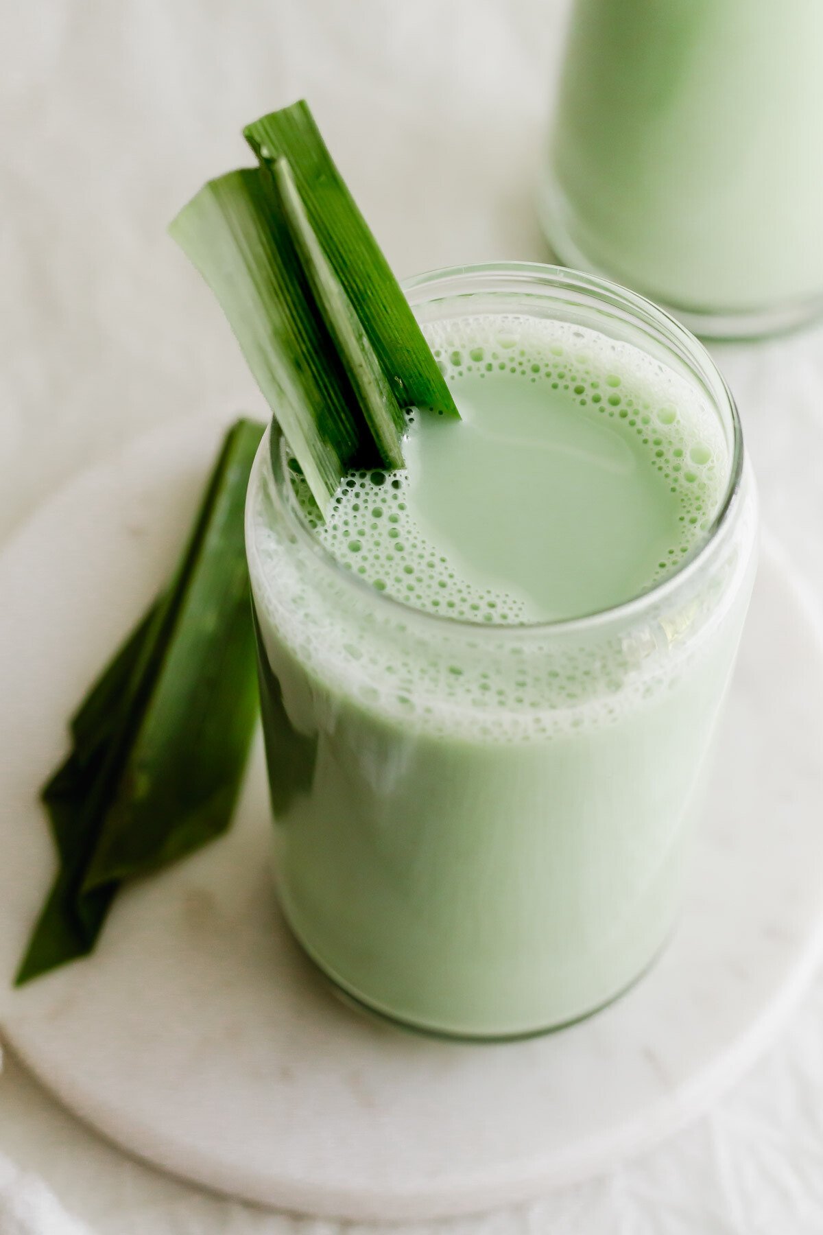 A glass of pandan soy milk on white round marble.