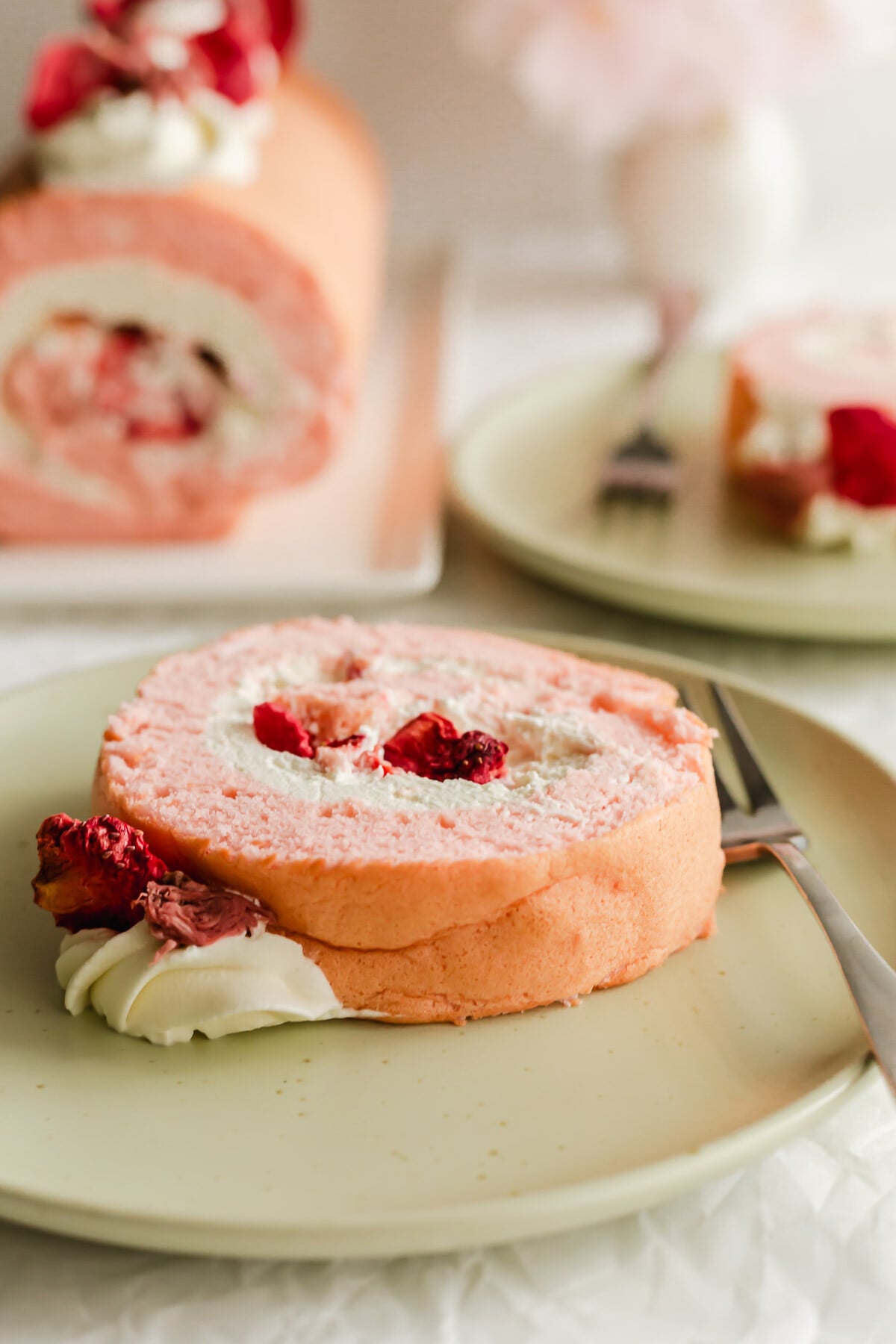 Slice of Cherry Blossom strawberry roll cake on a green plate with fork.