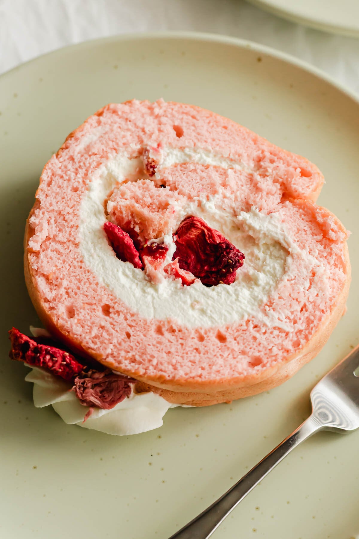 Close up of Cherry blossom strawberry roll cake on green plate with fork.