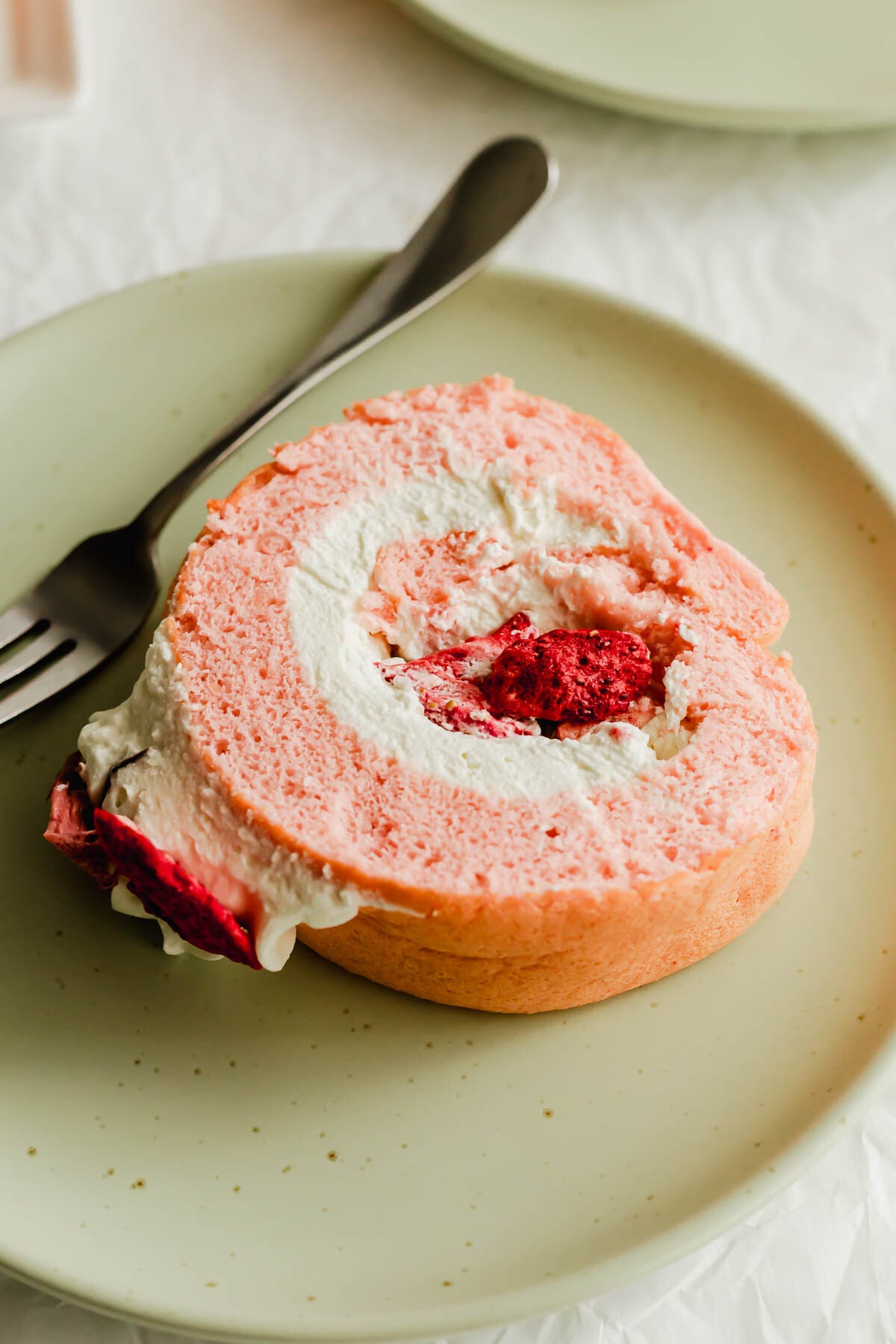 Close up of Cherry blossom strawberry roll cake on green plate with fork.