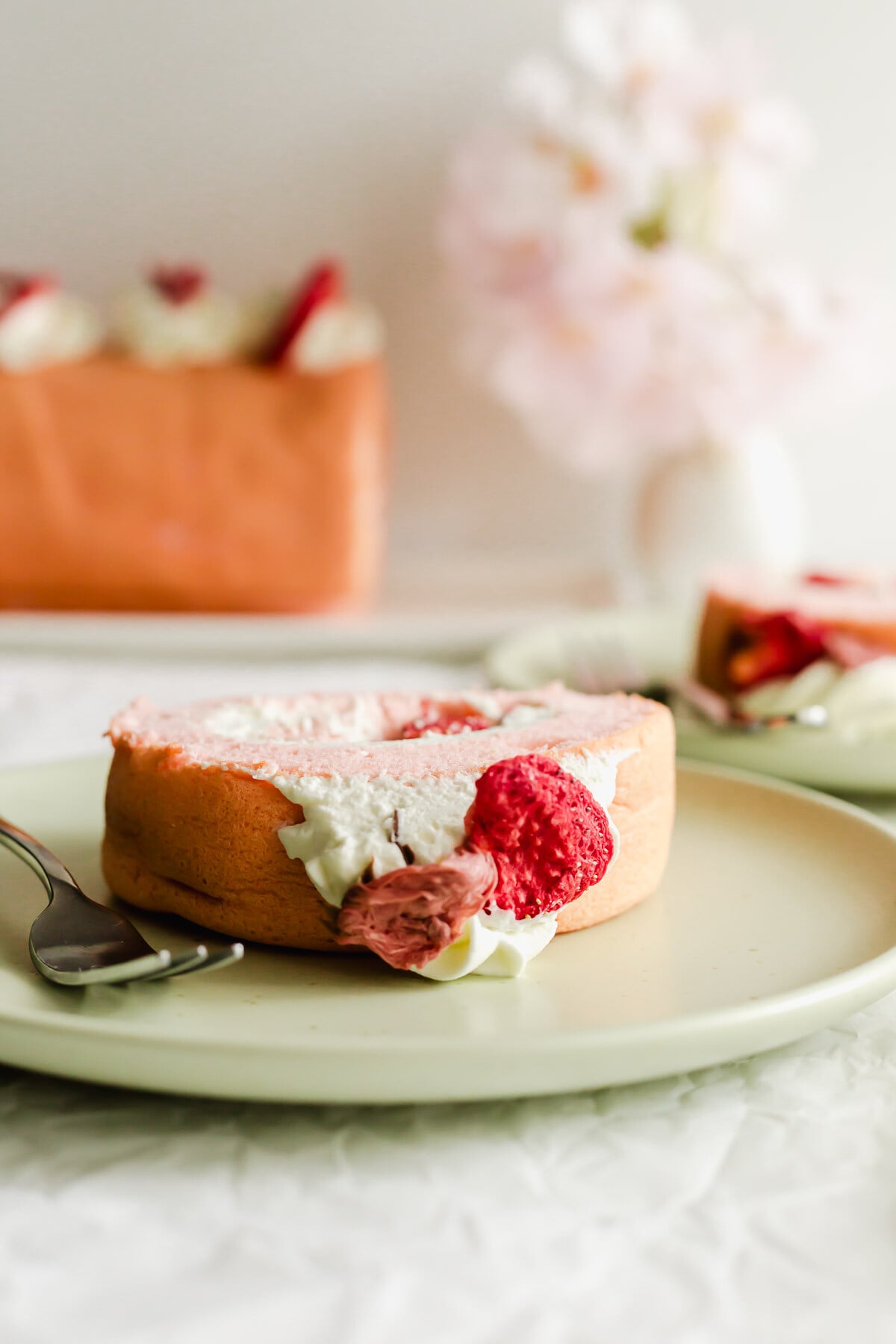 Close up of Cherry blossom strawberry roll cake on green plate with fork.