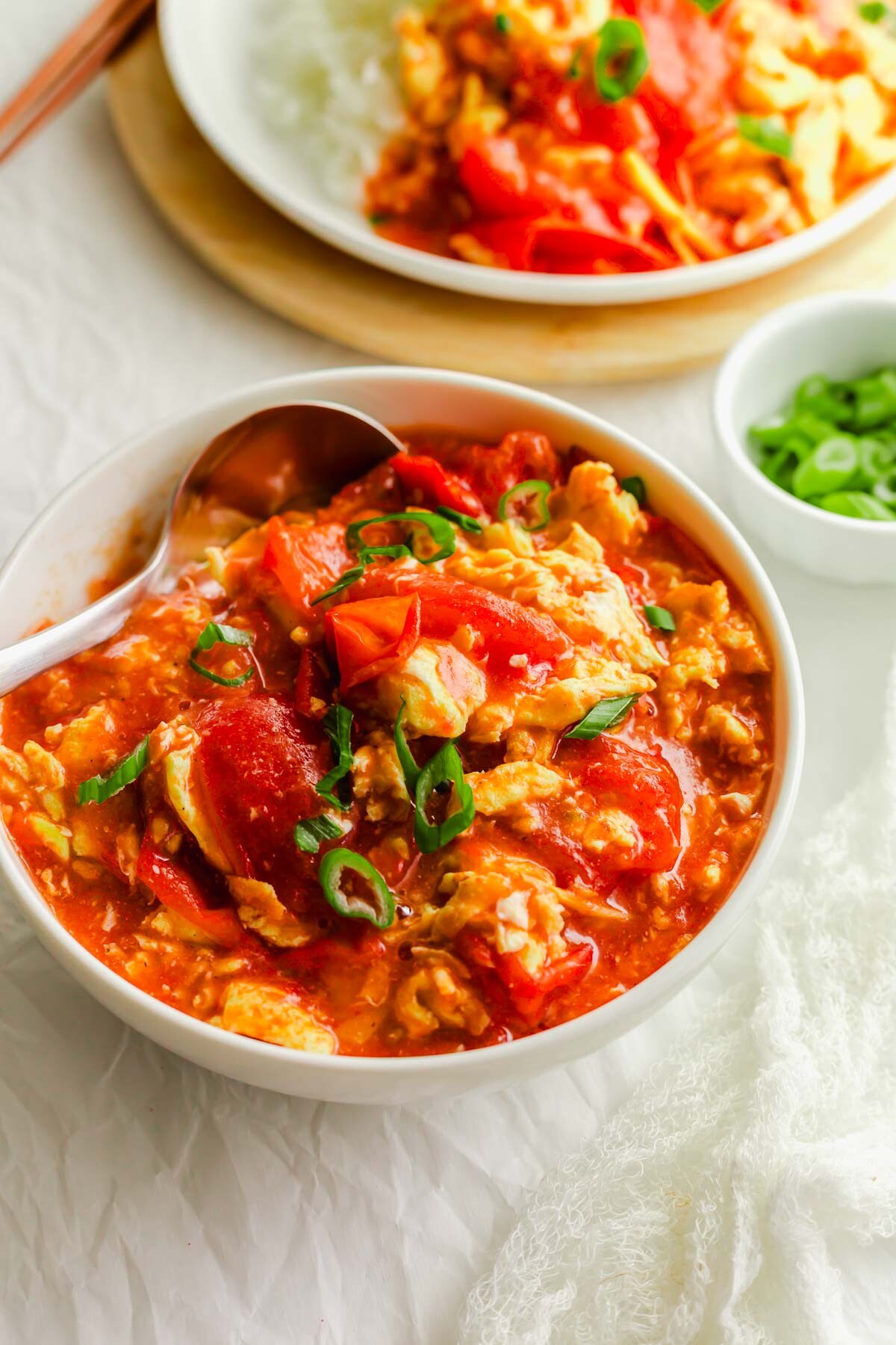 Chinese tomato egg in a white bowl with ladle.