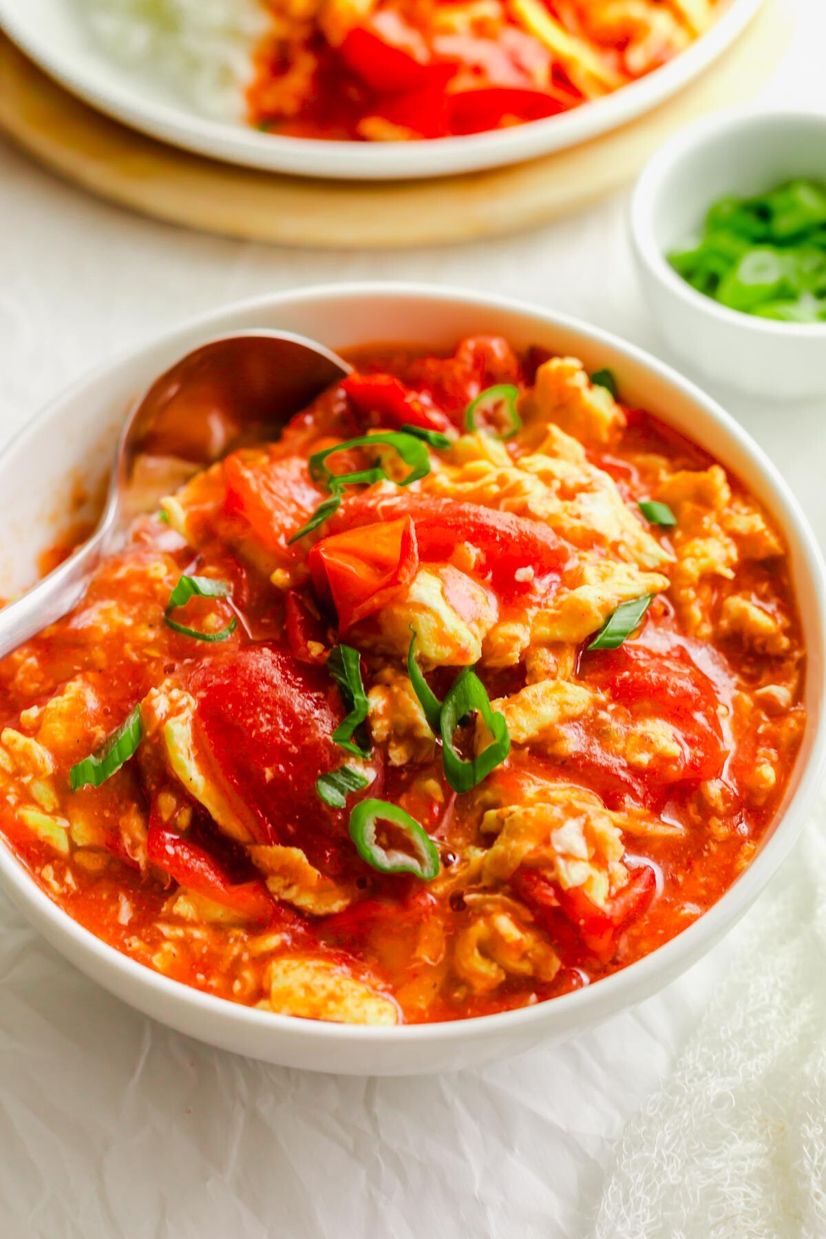Chinese tomato egg in a white bowl with ladle.