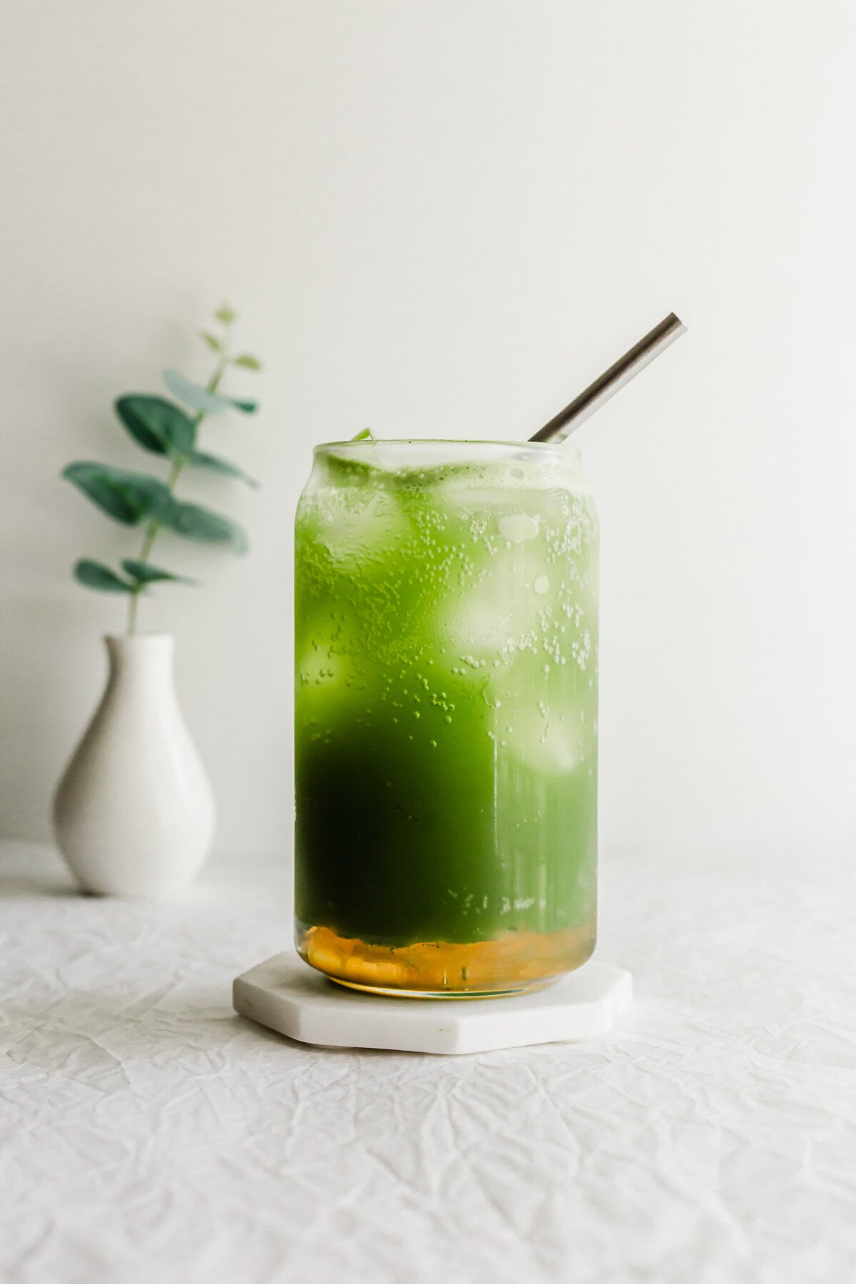 A matcha yuzu drink in a glass with a straw.