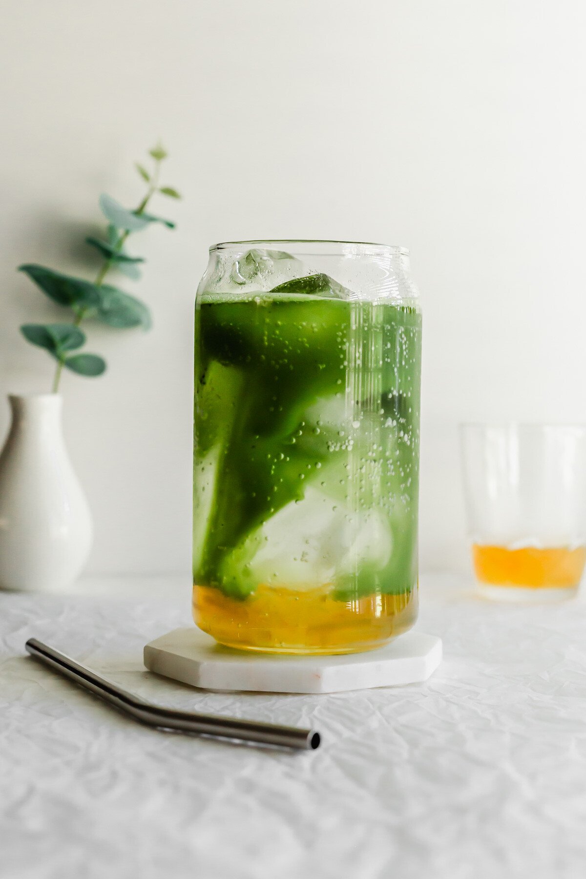A layered matcha yuzu drink in a glass with a straw on the side.