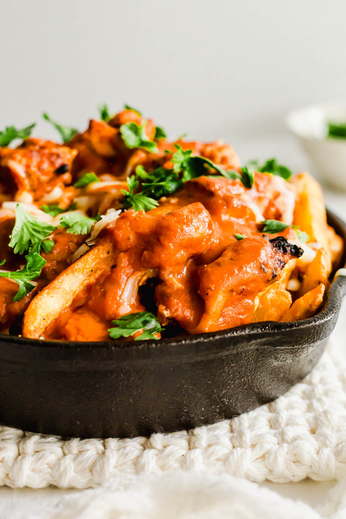 Close up of Butter chicken poutine in a black skillet.