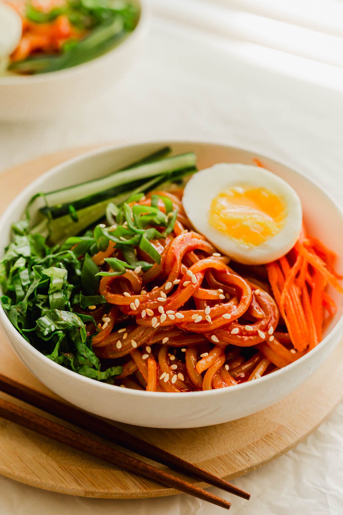 Korean spicy jjolmyeon noodles mixed with gochujang with toppings in a white bowl.