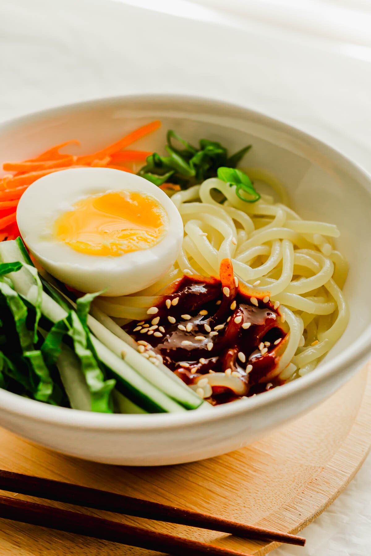 Korean spicy jjolmyeon noodles with toppings in a white bowl.