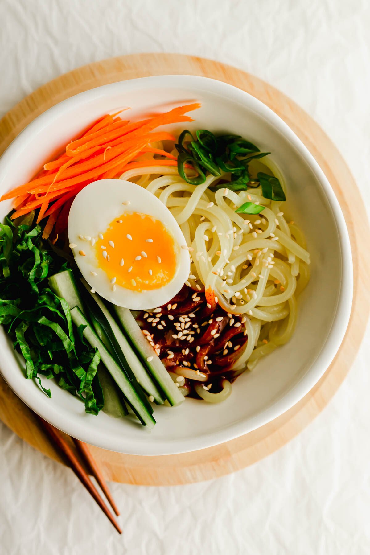 Korean spicy jjolmyeon noodles with toppings in a white bowl.