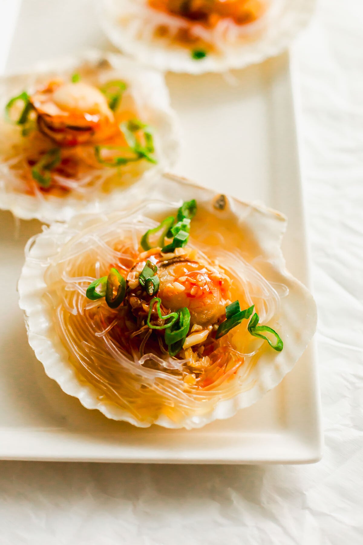 Steamed scallops on a half shell, on white plate.
