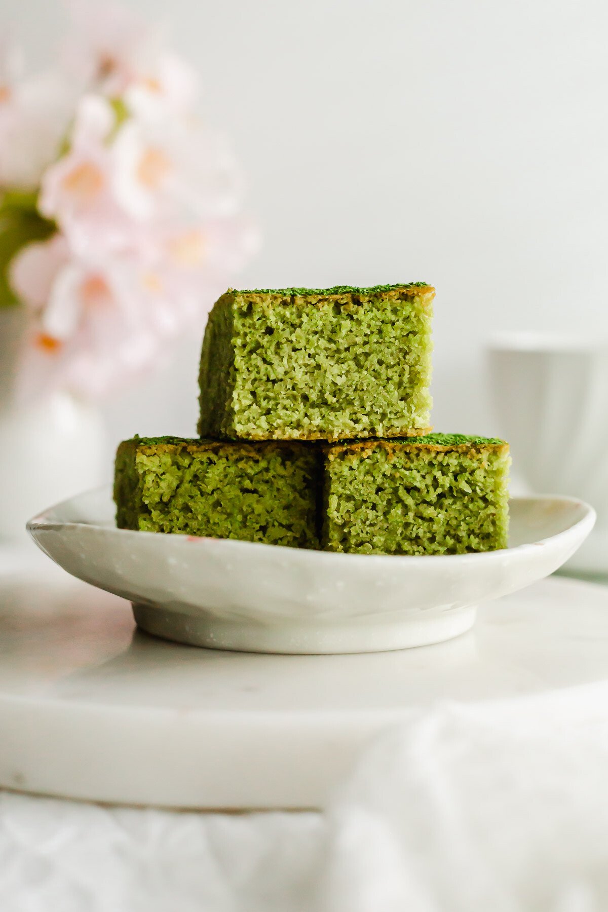 Matcha almond brownies stacked on a white plate.