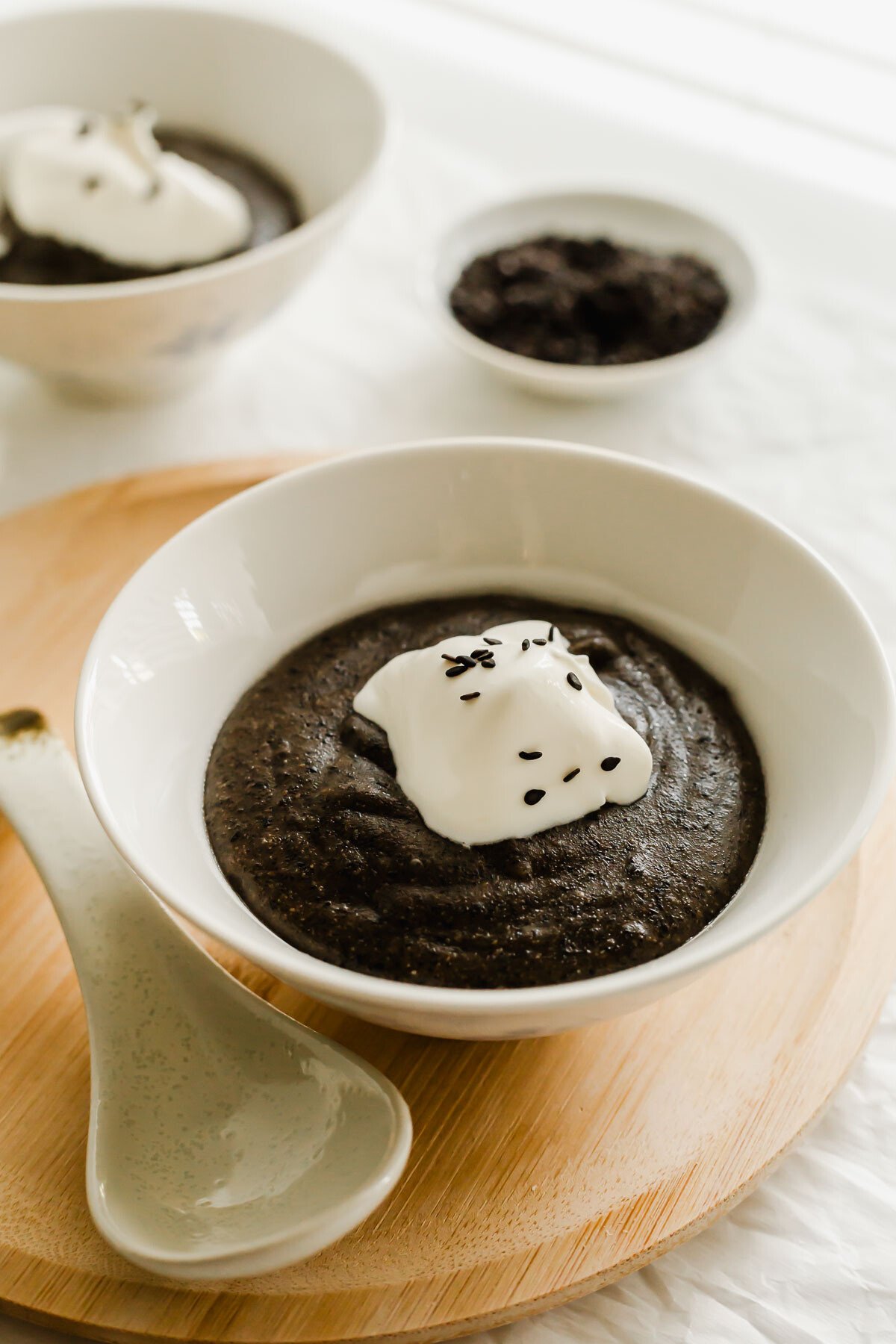 Black sesame paste in a white bowl, with a dollop of whipped cream and sesame seeds.