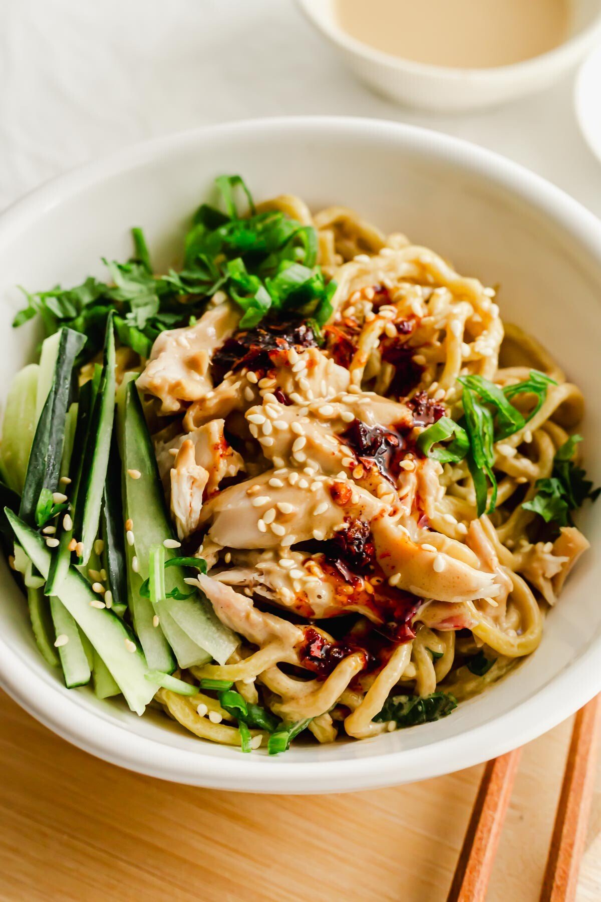 Chinese cold sesame noodles with chicken and chili oil in a white bowl.