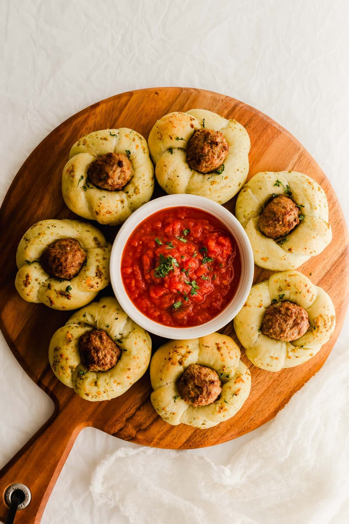 Garlic meatball knots on a wooden board, with a bowl of marinara sauce in the middle.