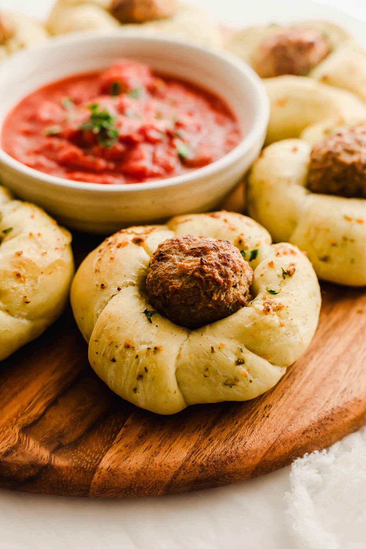 Garlic meatball knots on a wooden board, with marinara sauce in the background.