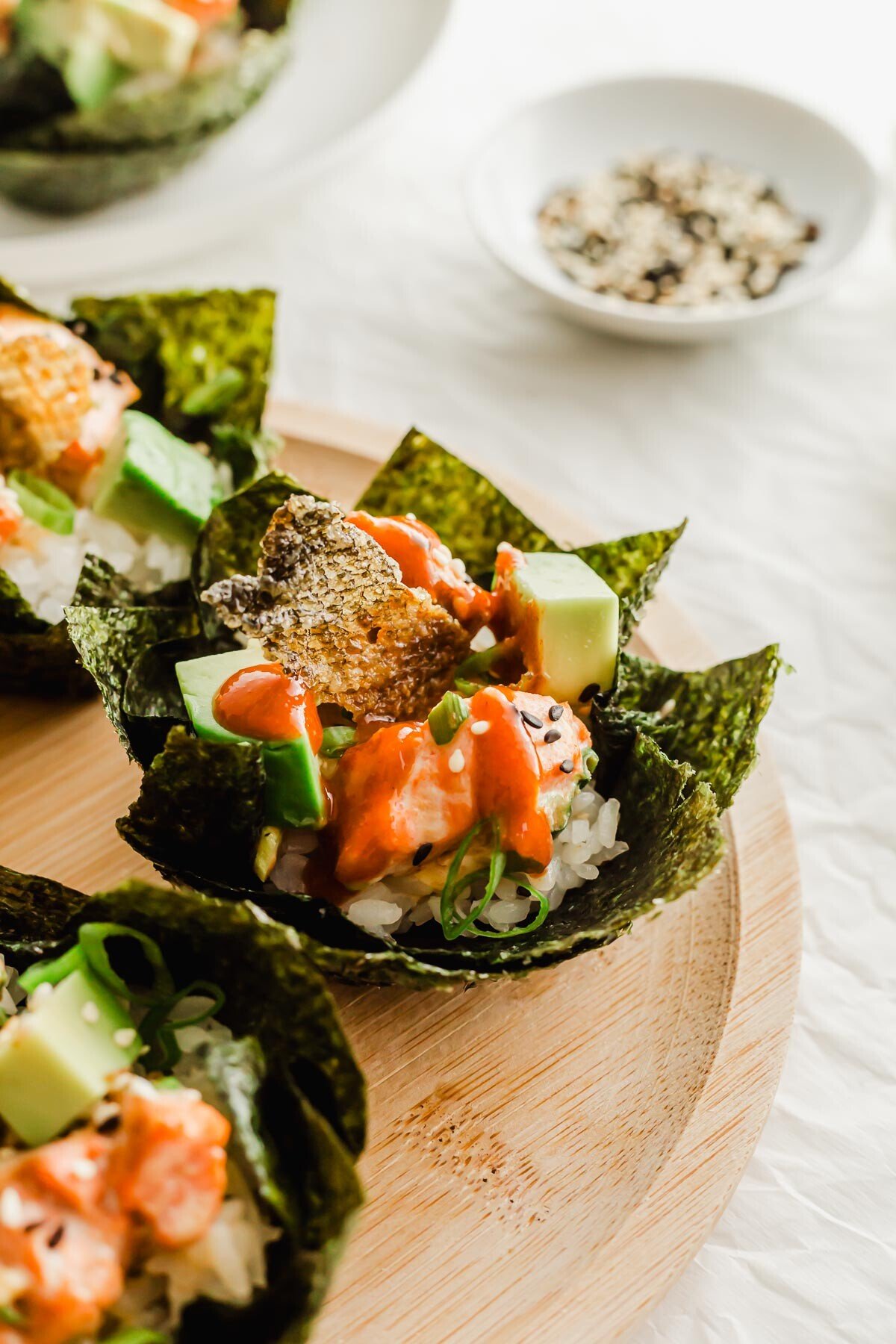 Baked salmon sushi cups topped with sriracha on a wooden plate.